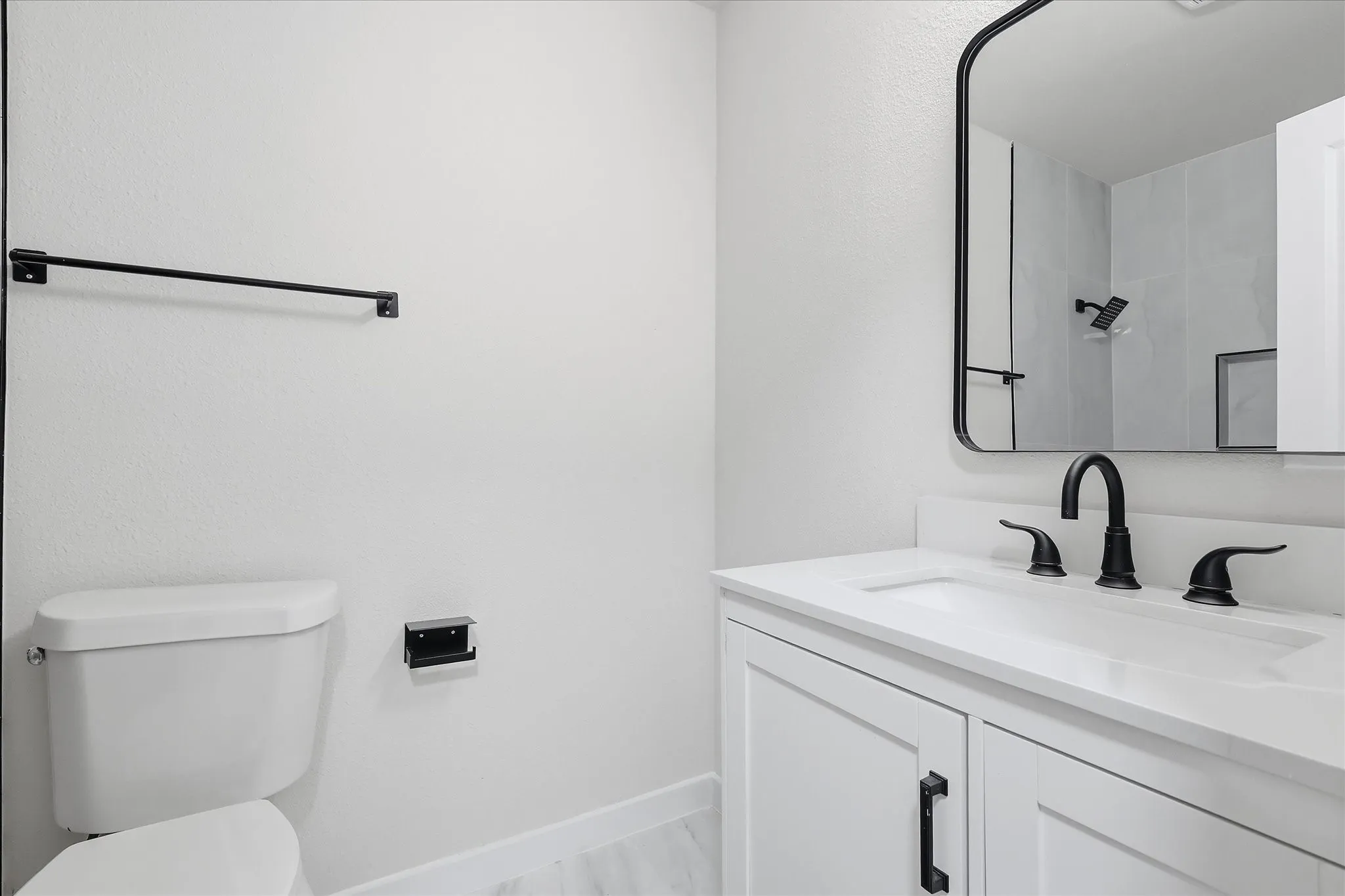 White vanity with a built-in sink, dark hardware, and a framed mirror