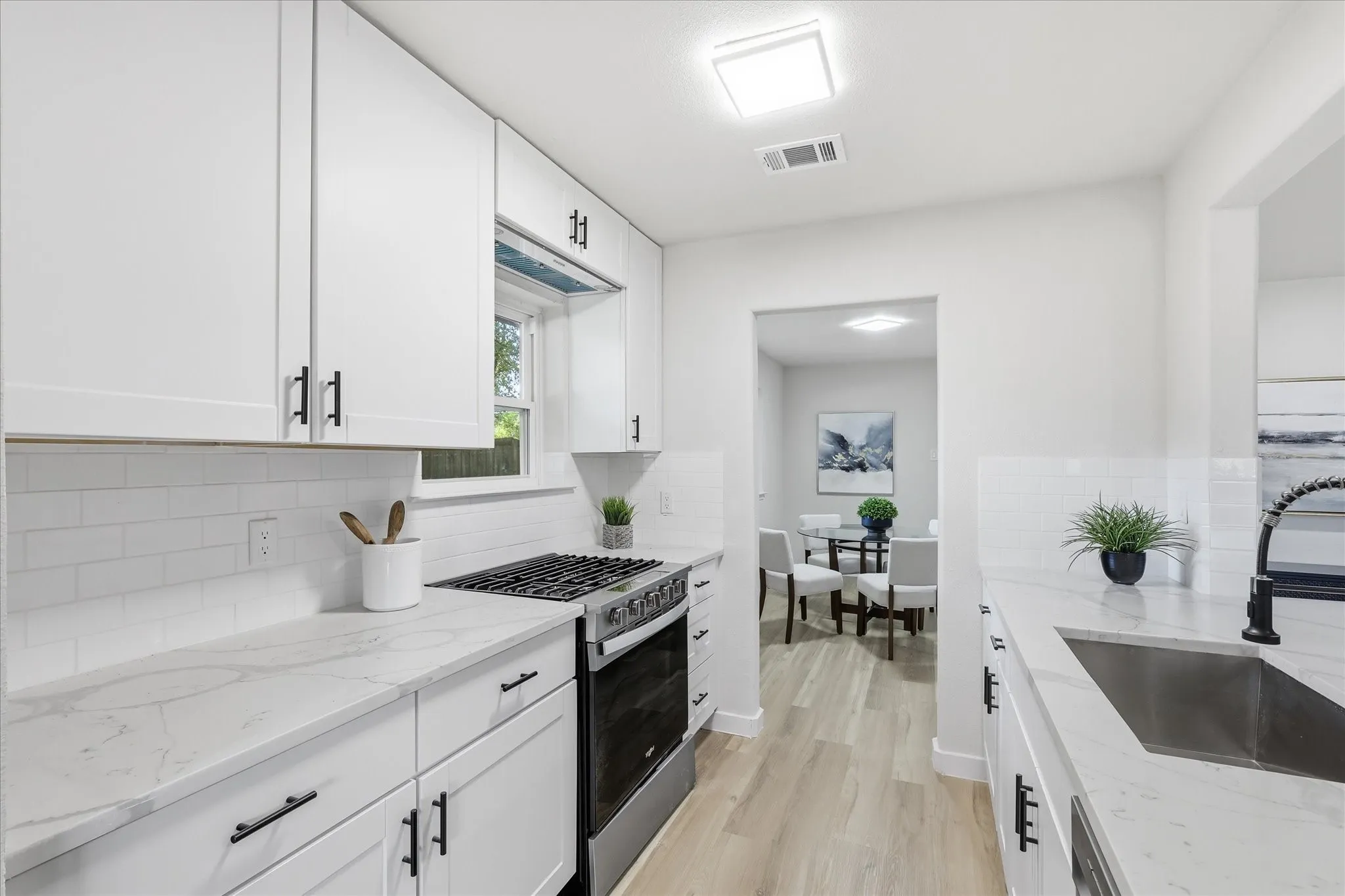 Bright kitchen featuring white shaker cabinetry, quartz countertops, subway tile backsplash, stainless steel gas range, and wood-finish flooring