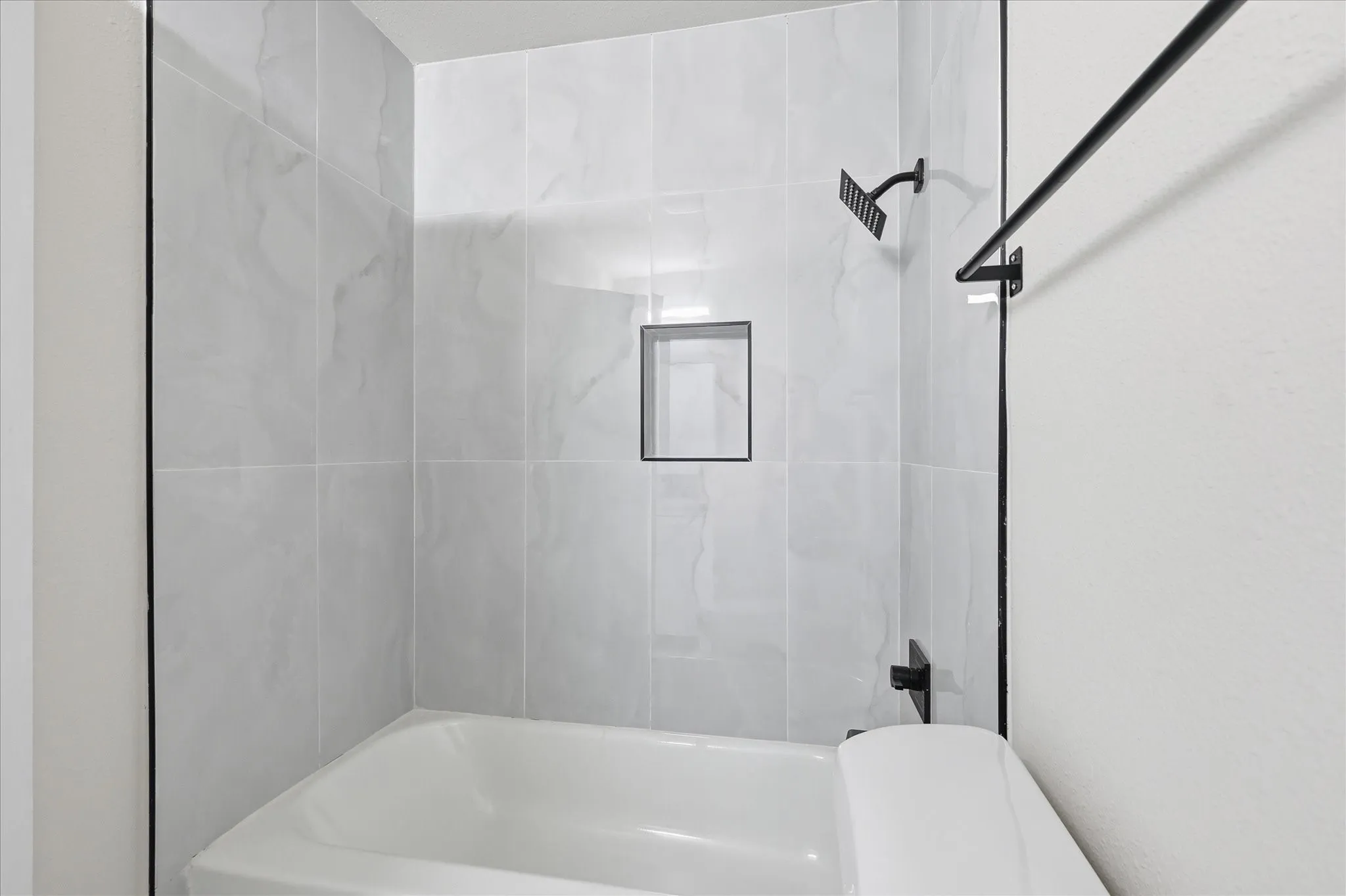Bathtub and shower combination featuring large format marble-look tile, matte black fixtures, and an integrated shower niche