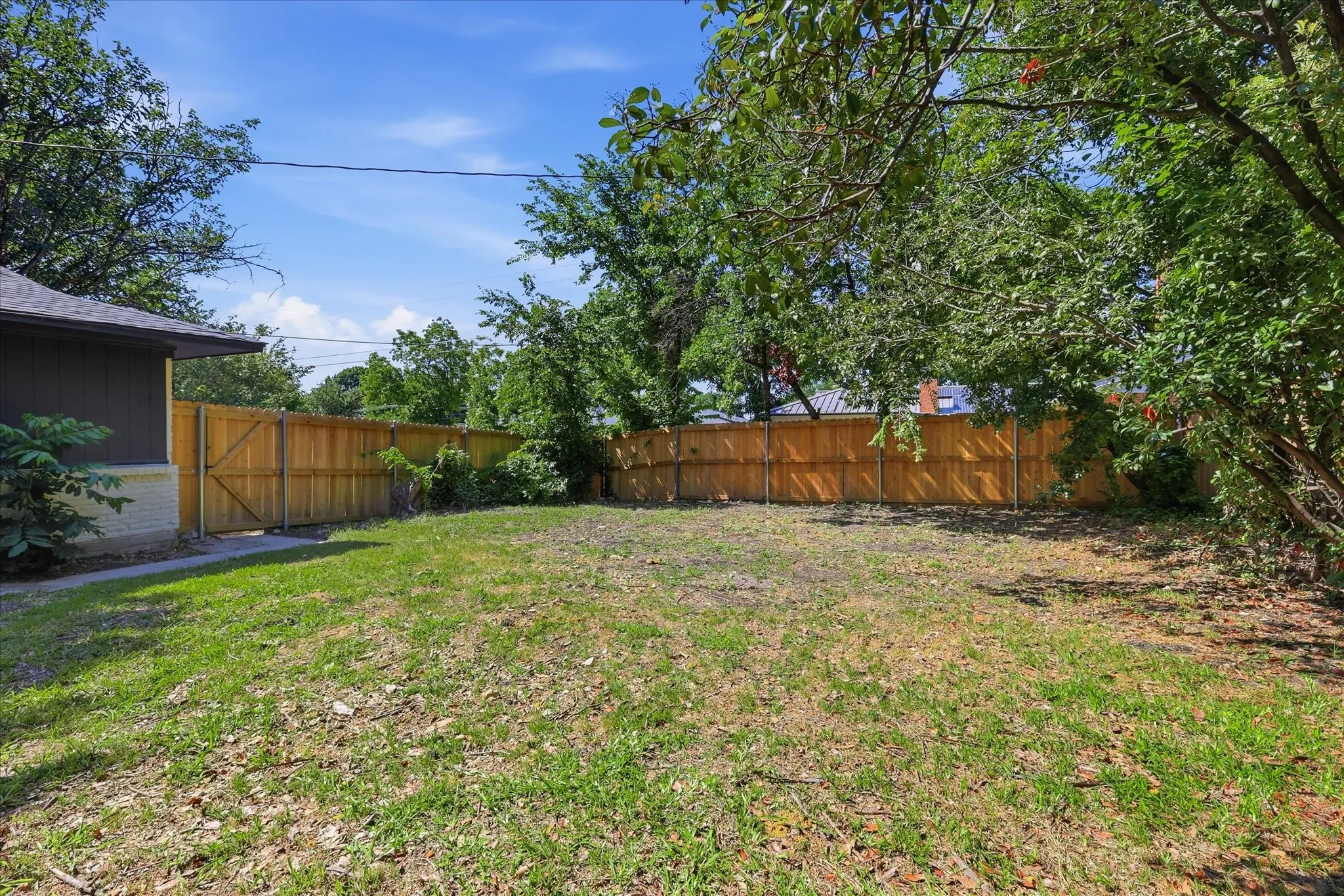 Expansive backyard featuring a natural grass lawn, mature trees, and a wooden privacy fence with a gate