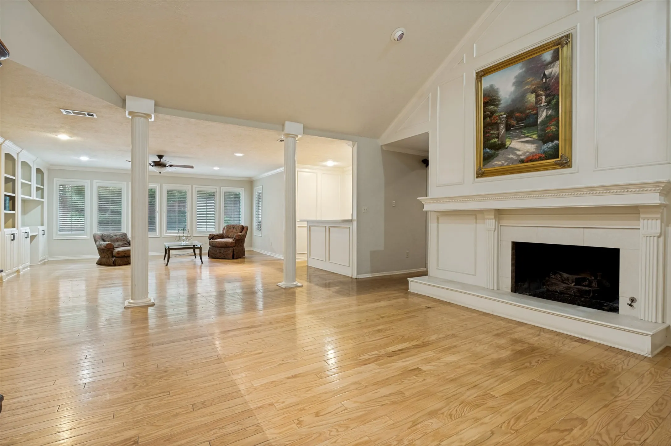 Spacious living area featuring light wood flooring, a fireplace with a white mantel and hearth, and vaulted ceilings