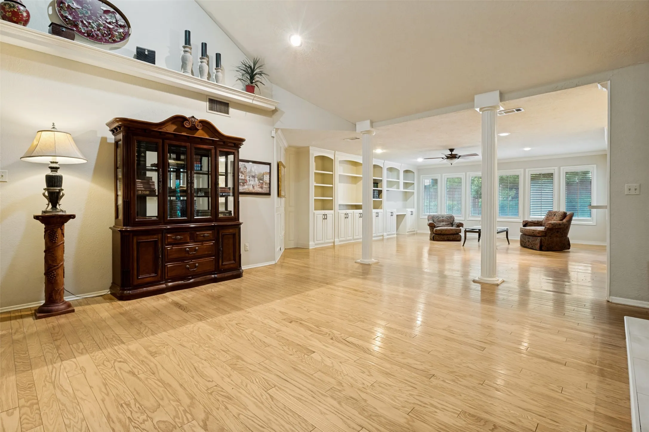 Hardwood flooring throughout a spacious room featuring a vaulted ceiling with a display shelf