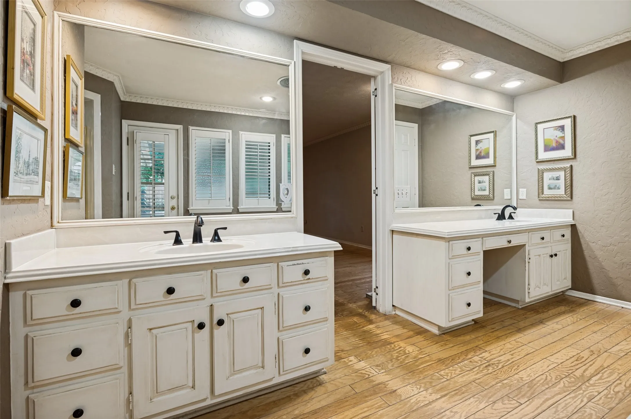 Bathroom vanity area featuring dual white cabinetry with black hardware, complementing white countertops, and expansive wall-mounted mirrors