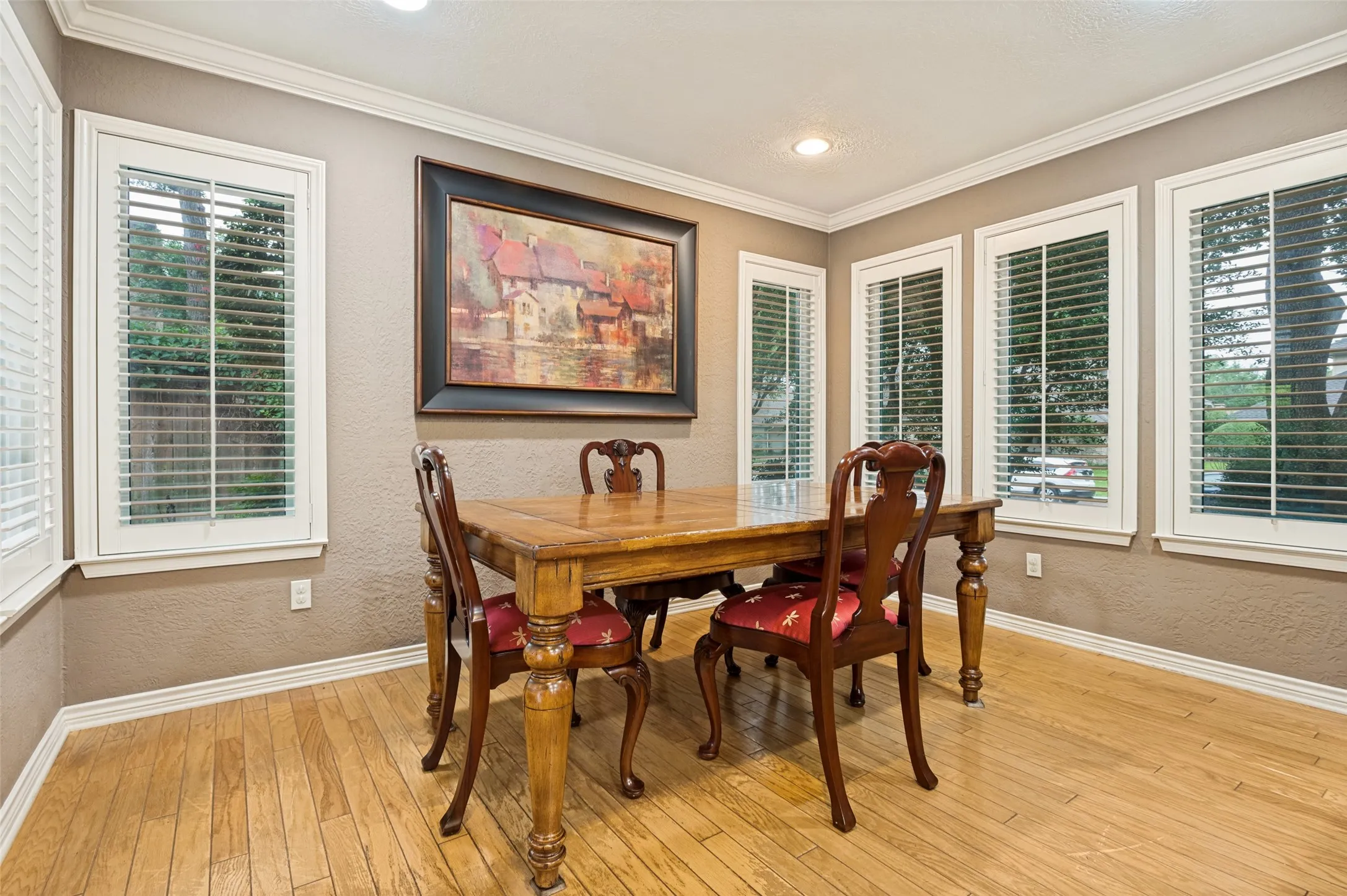 Dining area with wood-finish flooring, crown molding, recessed lighting, and multiple windows with white plantation shutters