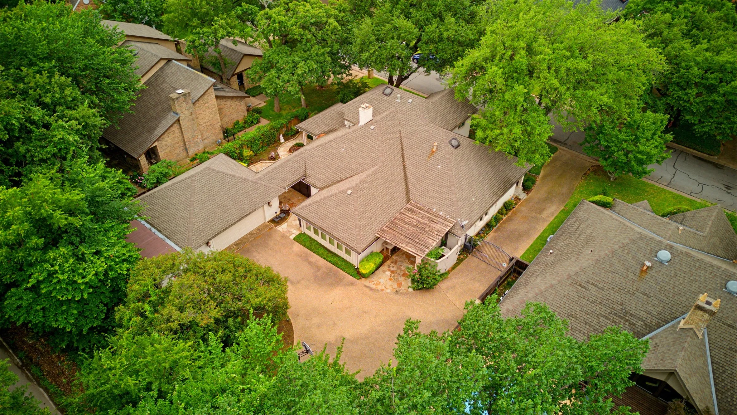 Expansive property featuring multiple structures, mature trees, a large paved driveway, and a covered entry