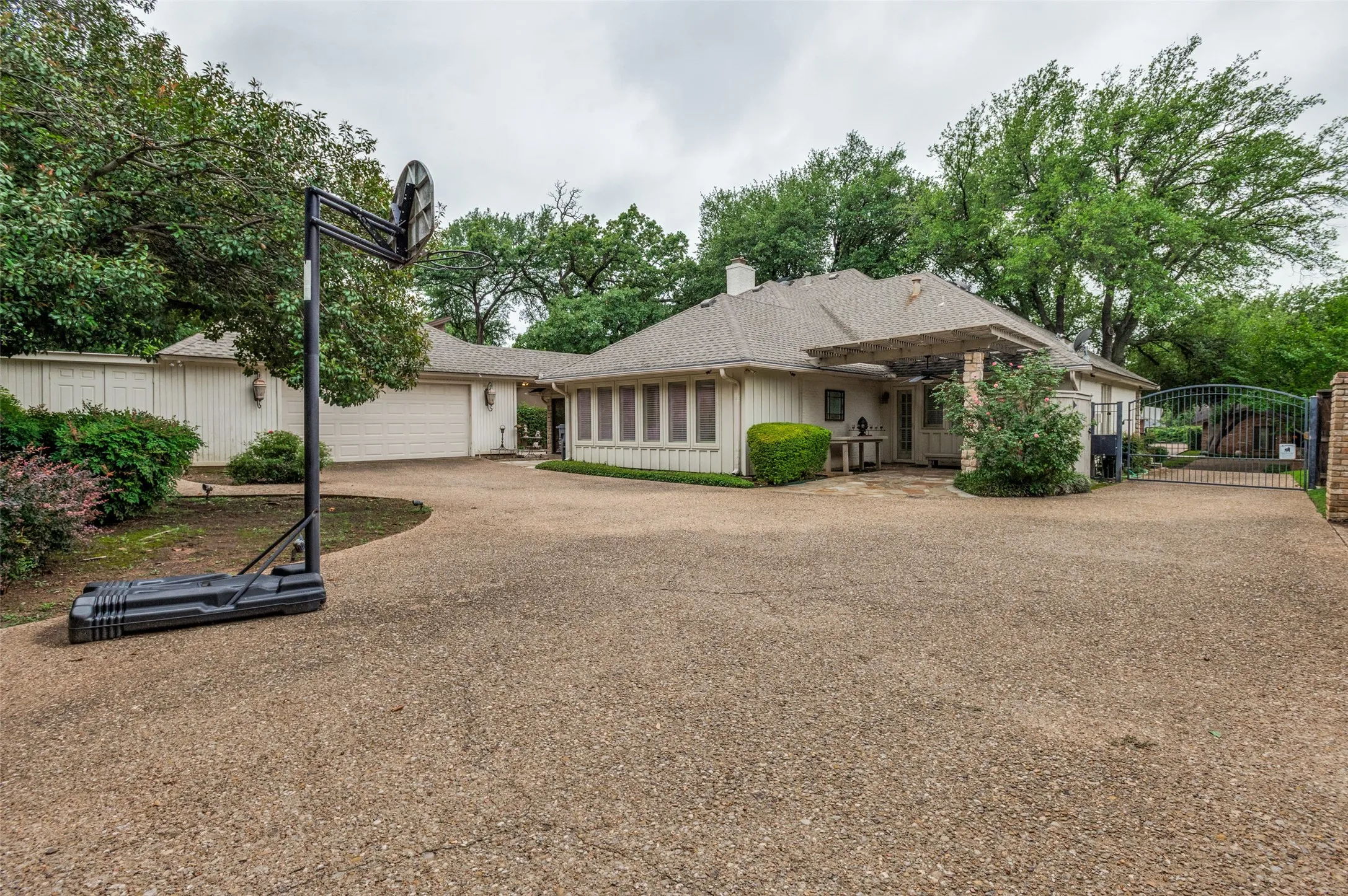 Expansive gravel driveway leading to a residence featuring a gated entrance, attached garage, and lush perimeter landscaping