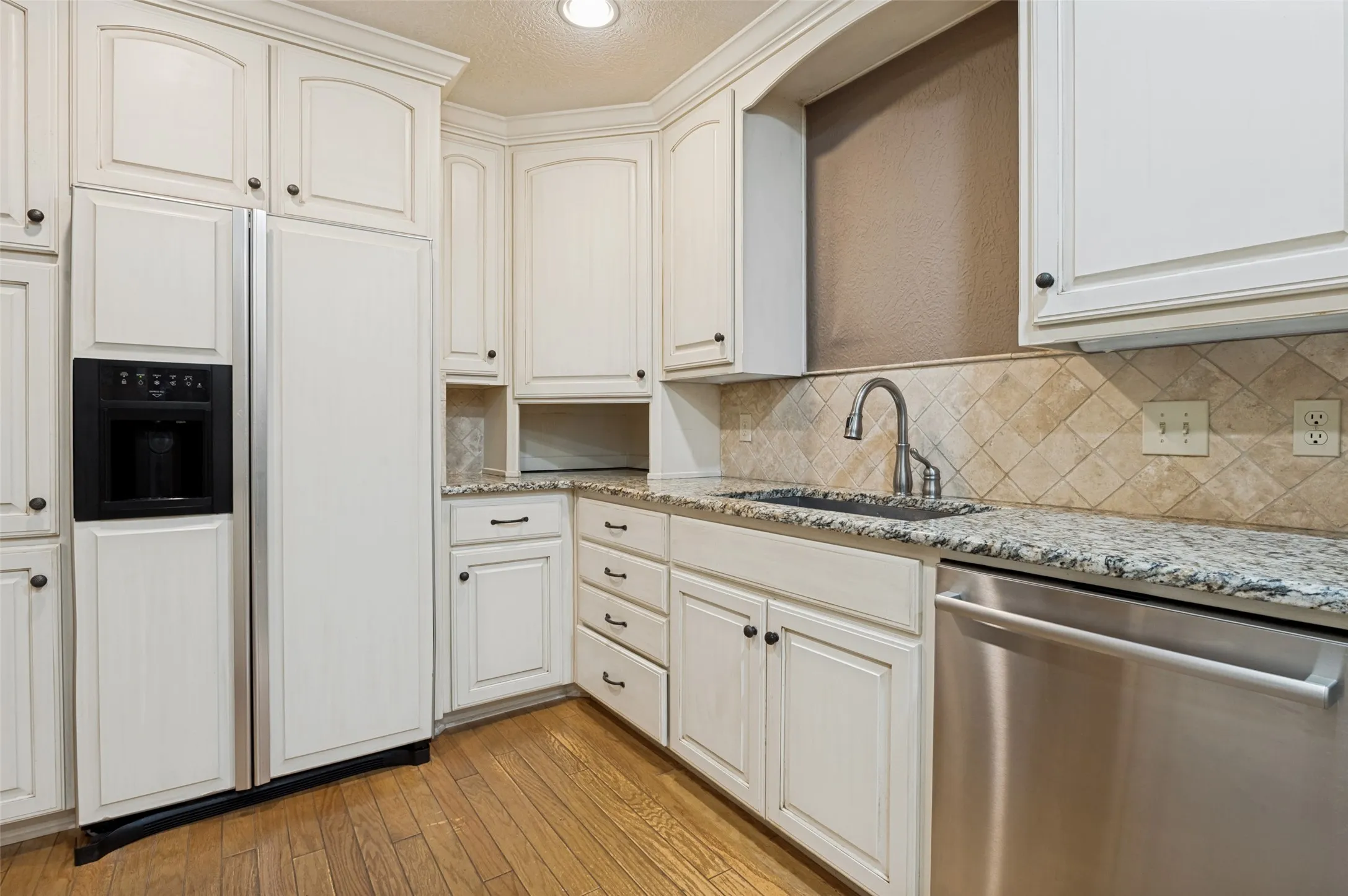 Kitchen featuring white cabinetry with dark hardware, granite countertops, a stainless steel dishwasher, and a tile backsplash