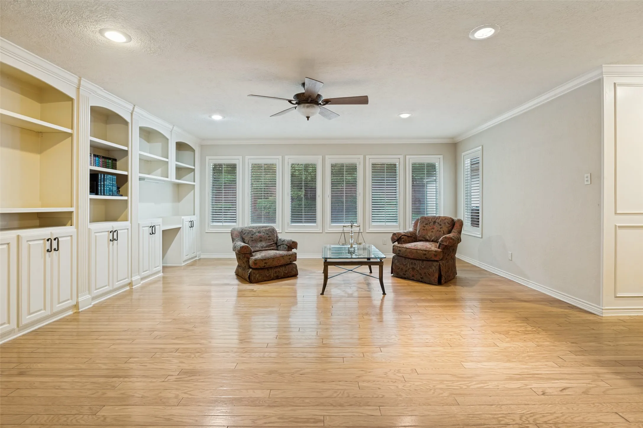Spacious room featuring extensive built-in cabinetry and shelving, recessed lighting, and wood-finish flooring