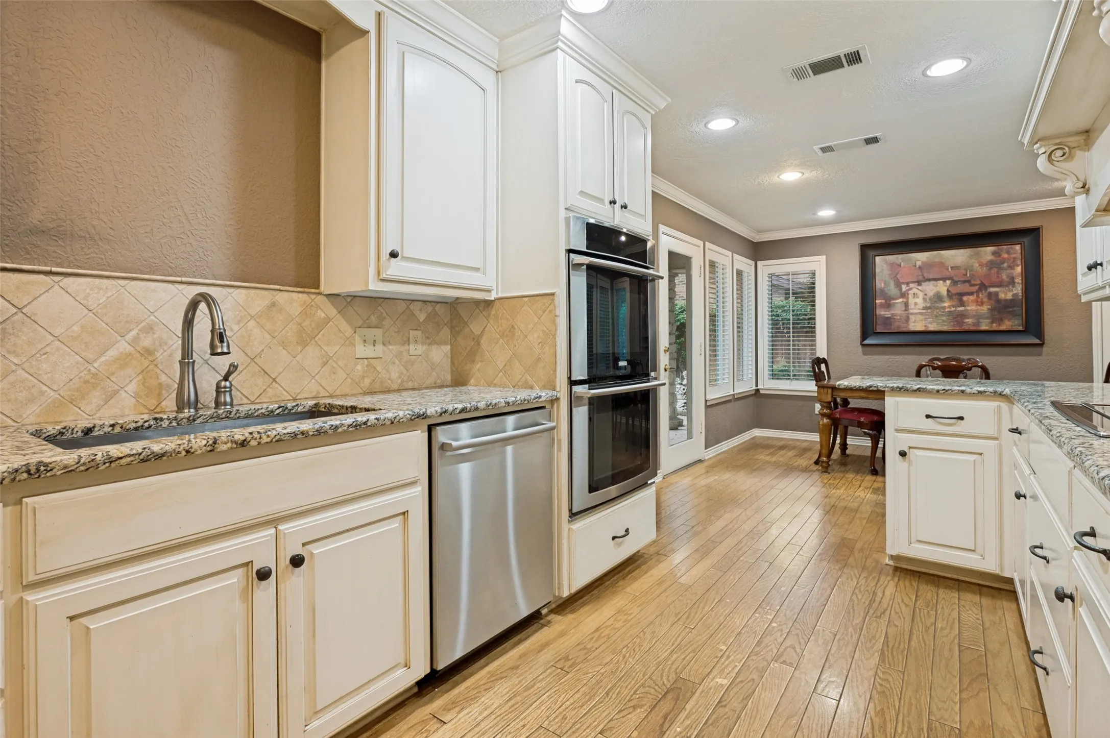 Kitchen featuring white cabinetry, granite countertops, tile backsplash, stainless steel dishwasher, and built-in double oven