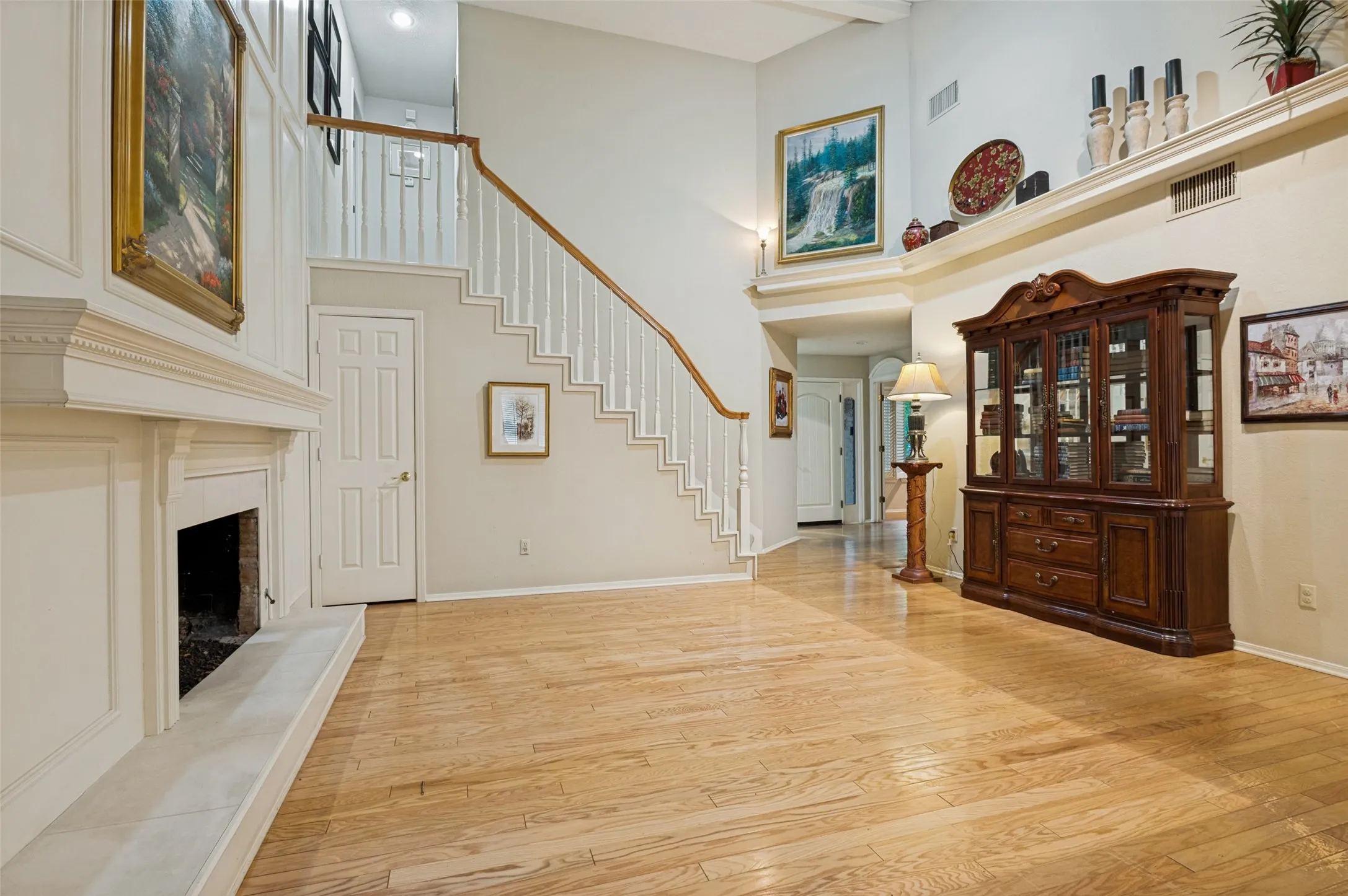 Spacious living area featuring light wood-finish flooring, a white mantel fireplace, and a staircase with white balusters