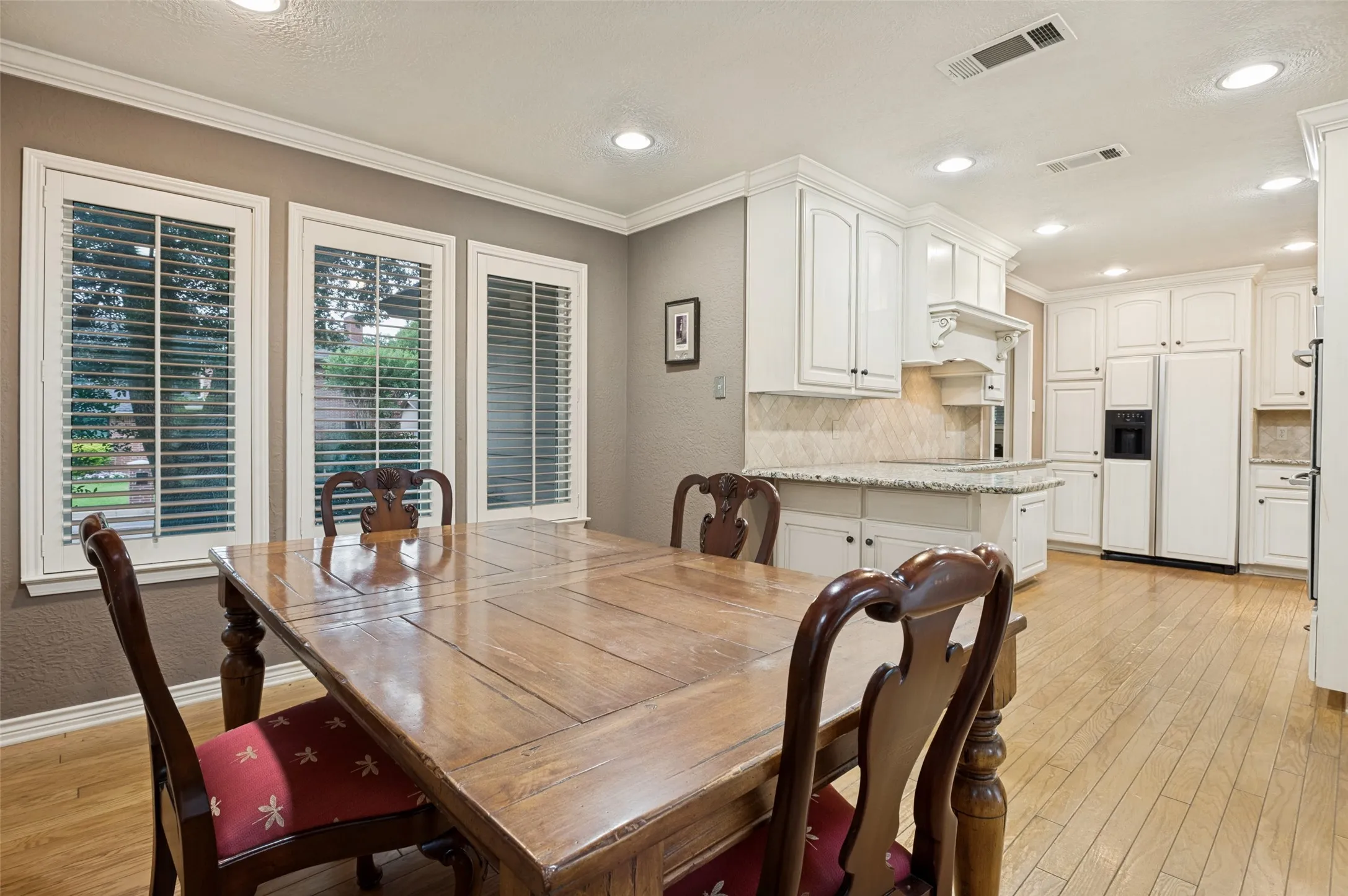 Kitchen and dining area featuring light wood-finish flooring, white cabinetry, recessed lighting, and a kitchen island with a stone-finish countertop