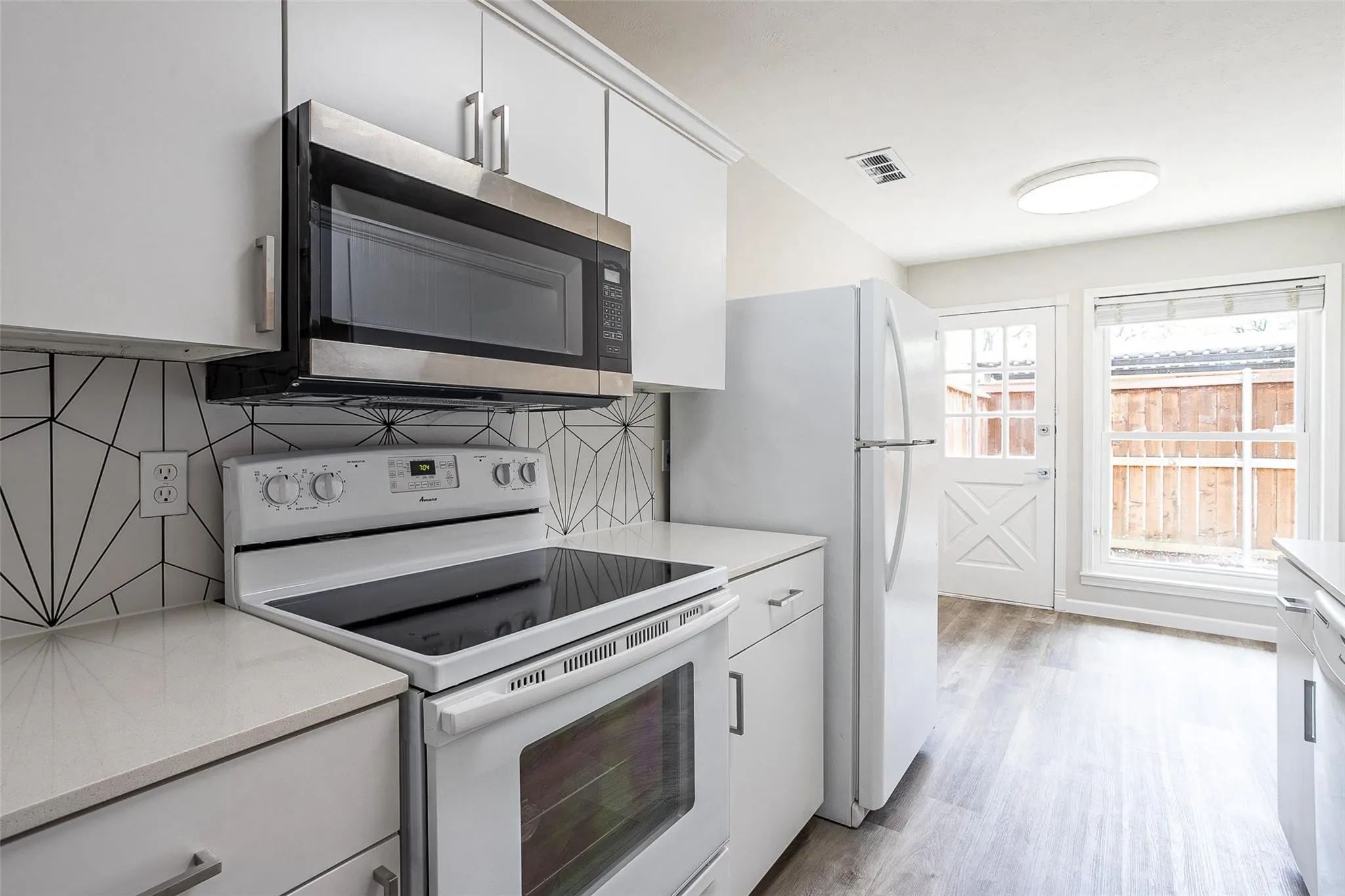 Kitchen featuring white cabinetry, light-toned countertops, a stainless steel over-the-range microwave, a white electric range, and geometric tile backsplash