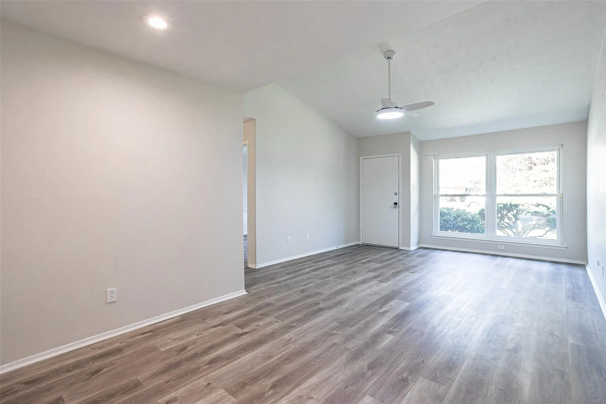 Spacious living area featuring wood-finish flooring, a contemporary ceiling fan with integrated lighting, recessed lighting, and large windows providing ample natural light