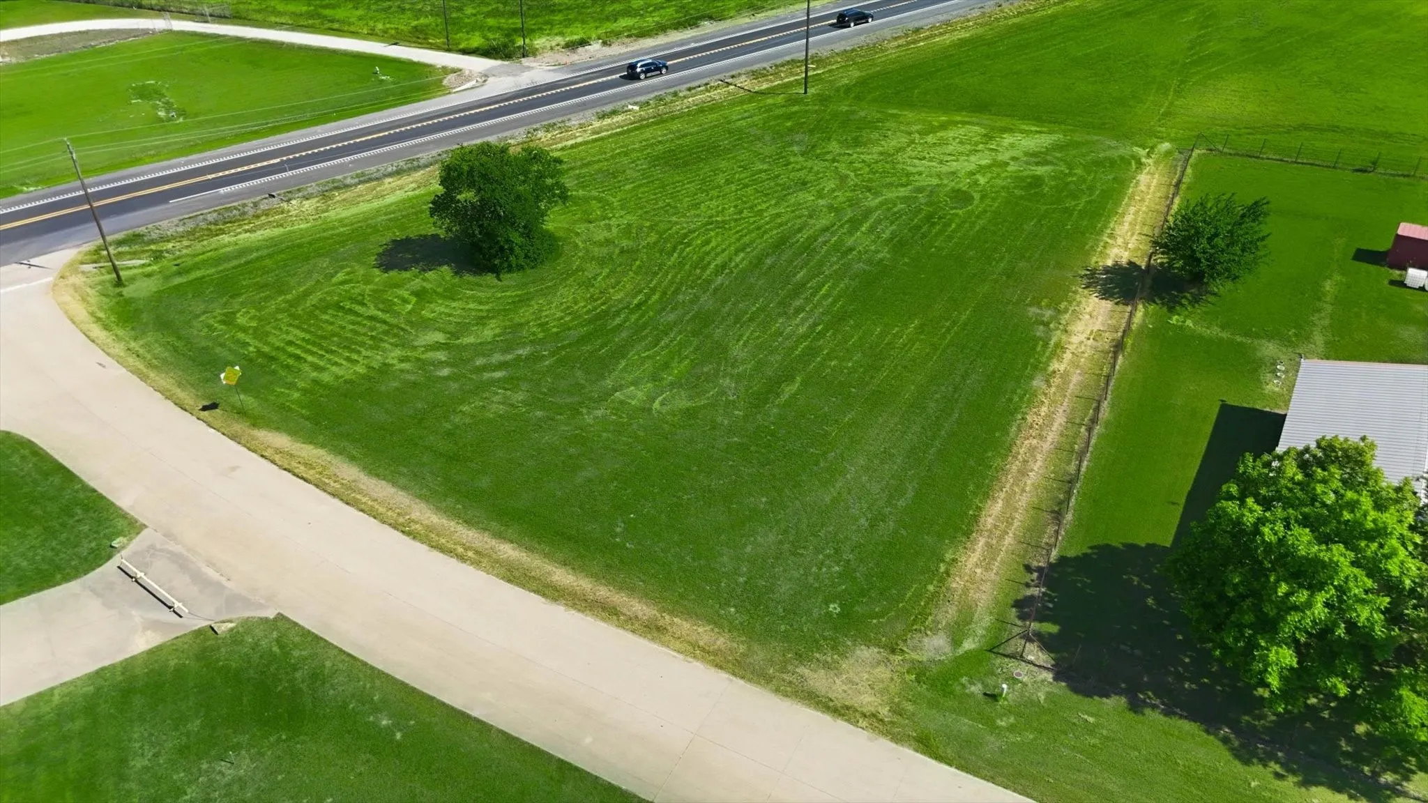 Expansive green lot featuring a paved road frontage, established tree, and clear property lines