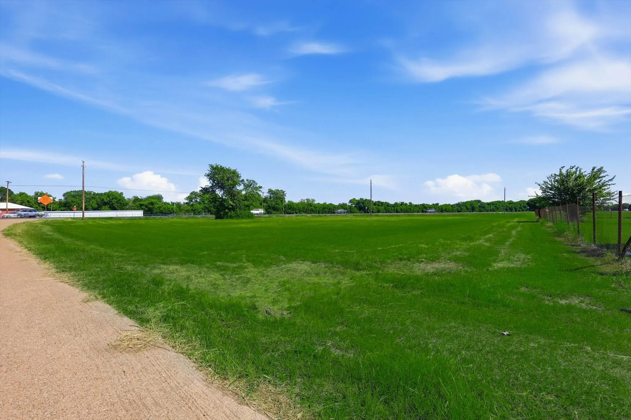 Expansive grass lot featuring a partial wire fence and scattered mature trees