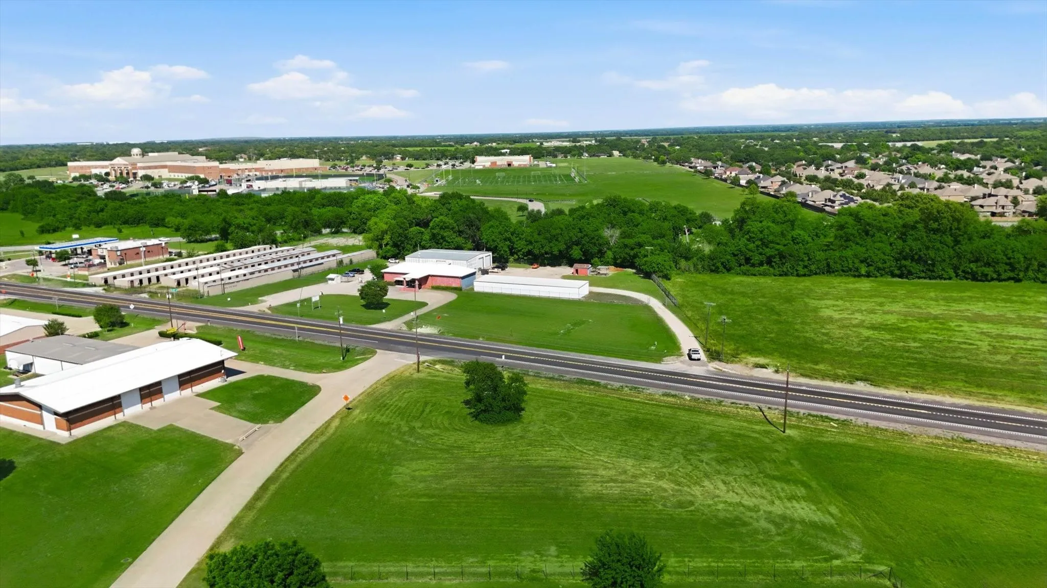 Expansive green space featuring a paved road, scattered commercial buildings, and distant residential developments