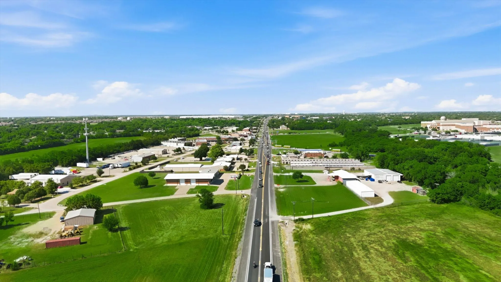 Expansive aerial perspective showcasing a straight highway traversing a landscape with green fields and scattered buildings
