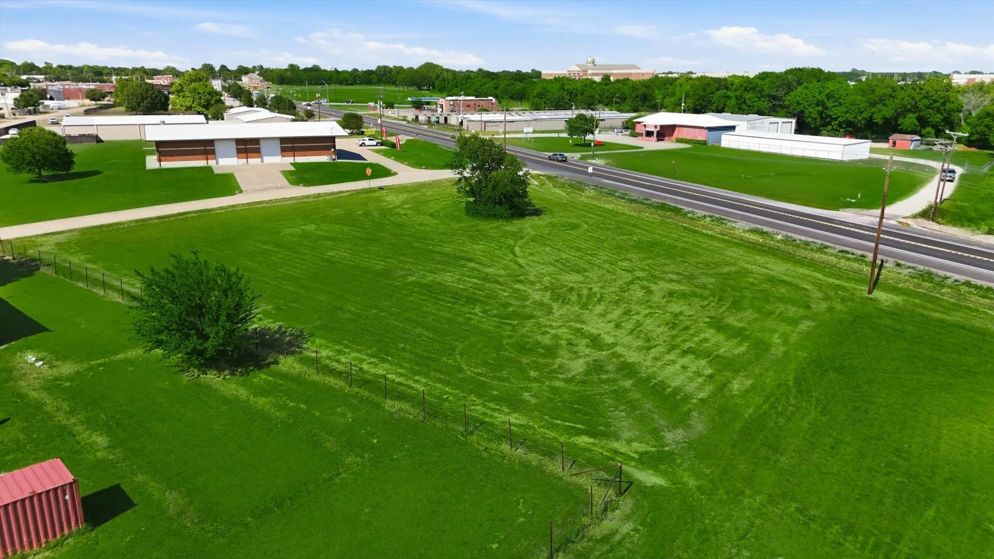 Expansive green space with perimeter fencing, mature trees, and direct road frontage