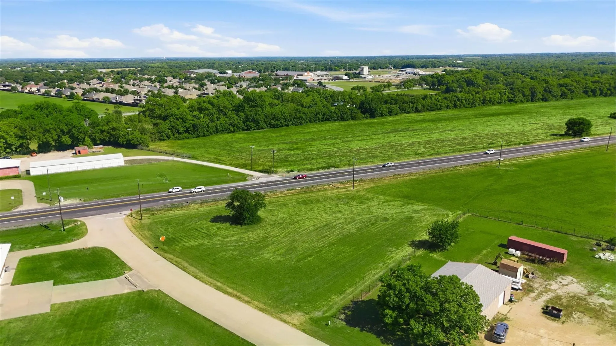 Expansive green fields bordering a paved road, with multiple structures present