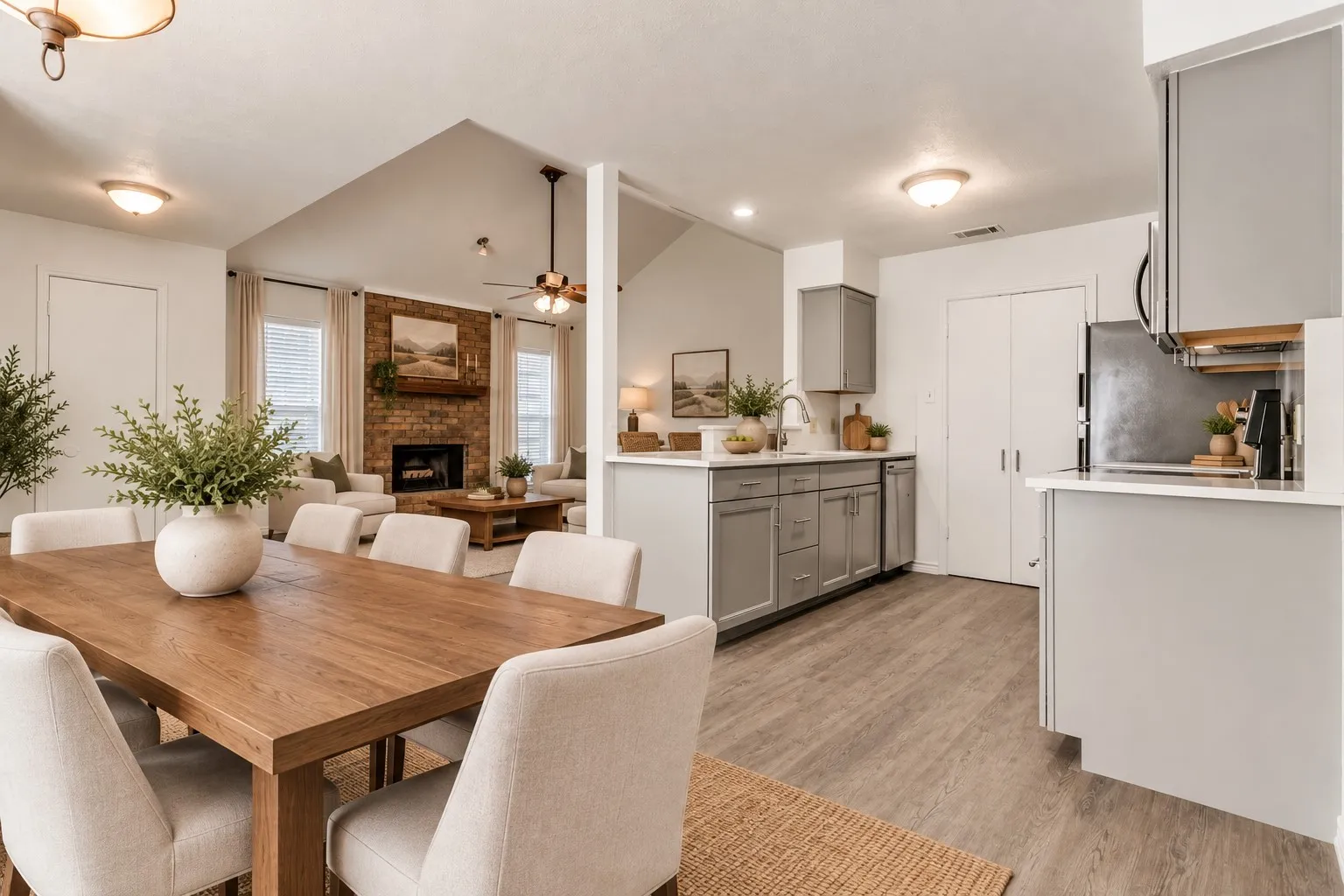 Open concept dining and kitchen area with wood-finish flooring, vaulted ceilings, and a brick-faced fireplace; virtually staged