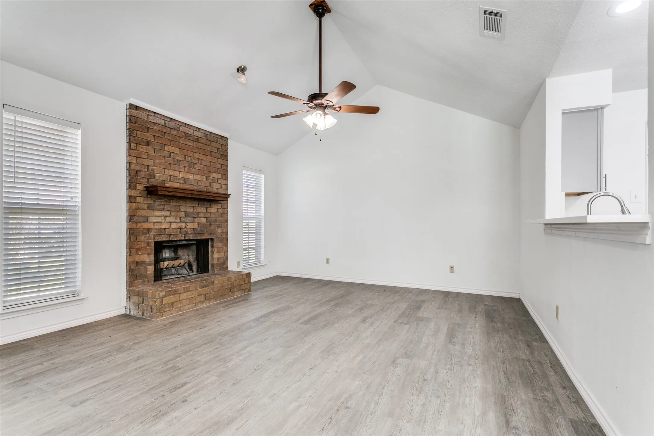 Spacious living area featuring a vaulted ceiling and a wood-burning brick fireplace with a wood mantel