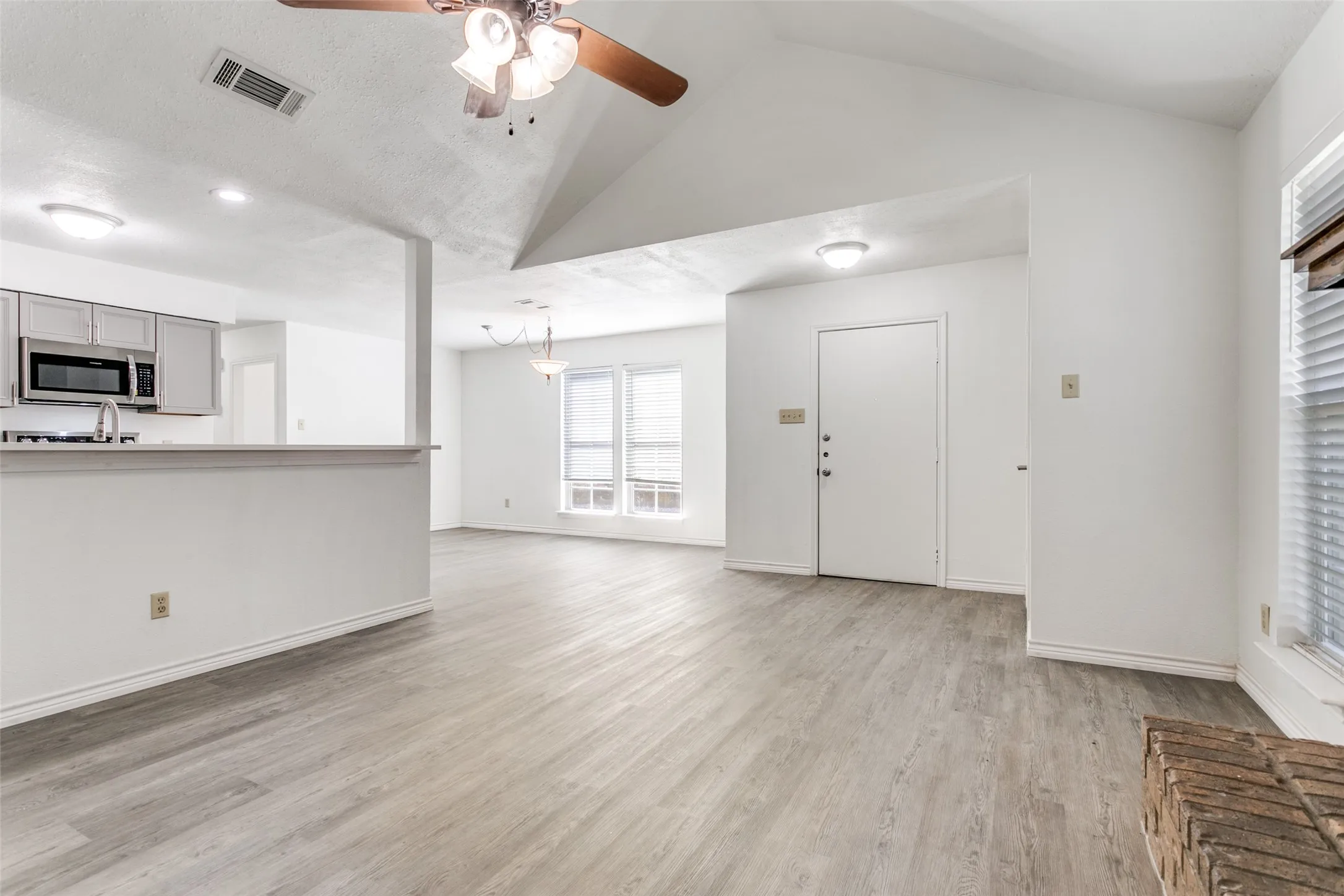 Spacious interior featuring wood-finish flooring, vaulted ceilings, and large windows with blinds