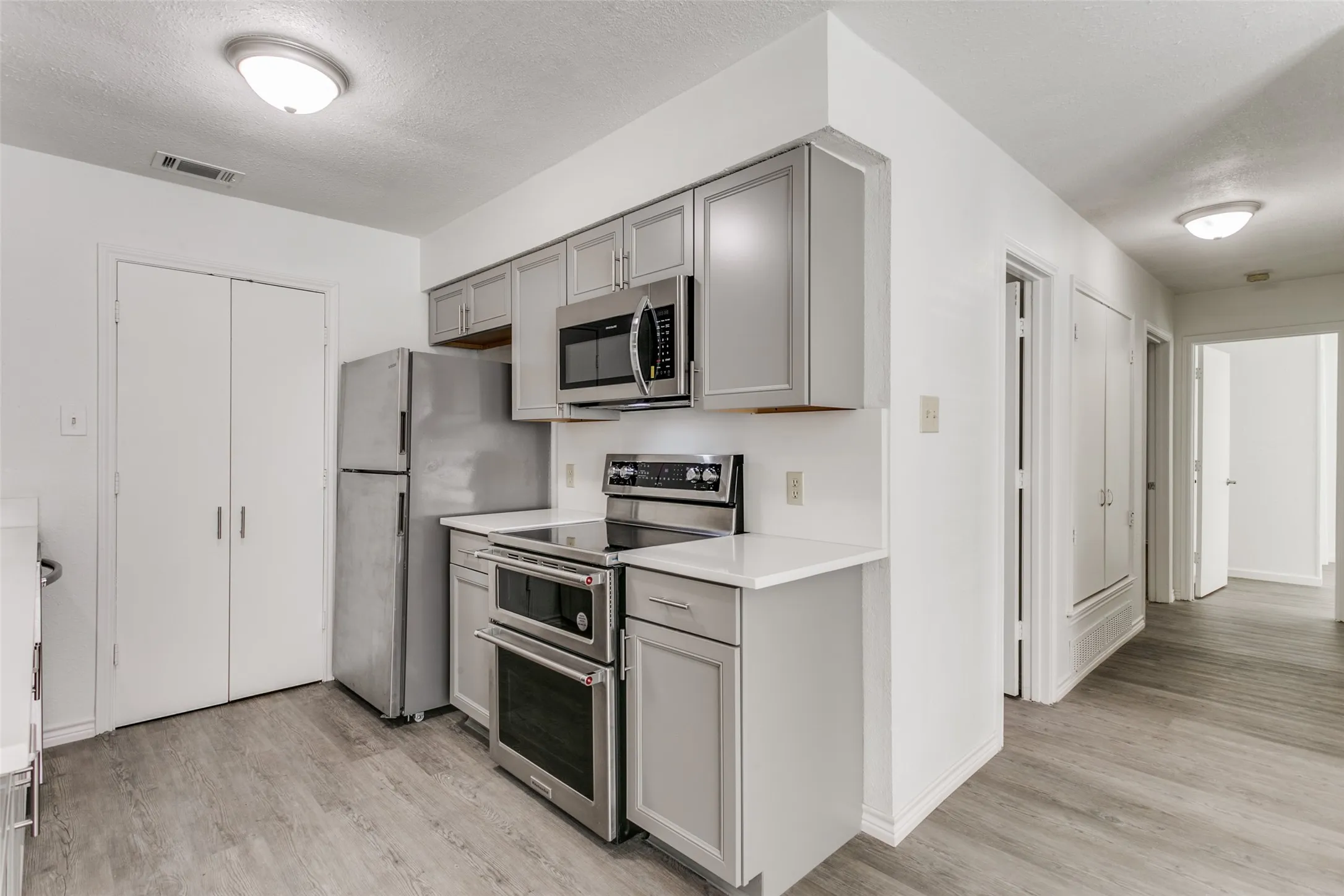 Kitchen featuring gray cabinetry, stainless steel appliances, white countertops, and wood-finish flooring