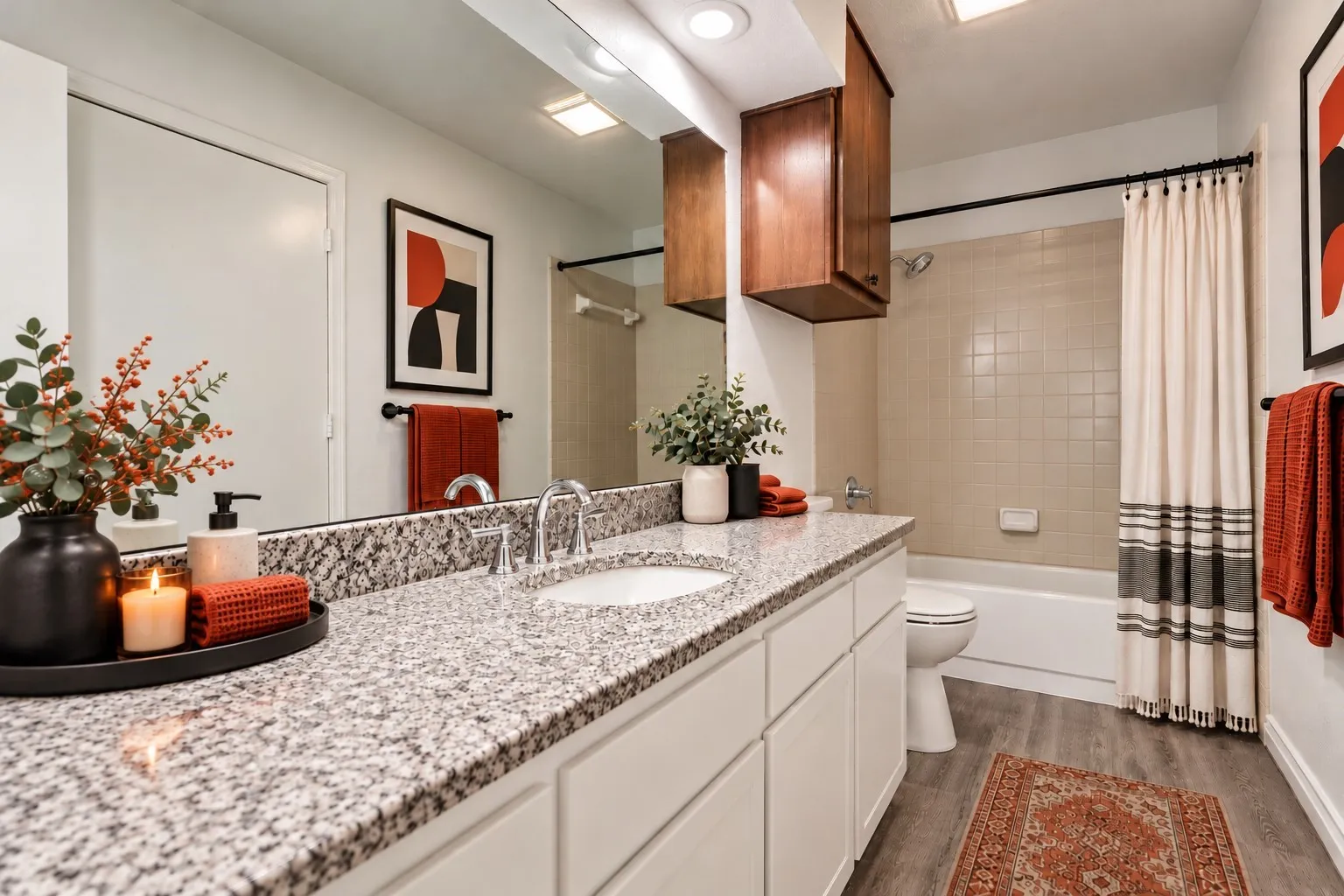 Granite-style countertop, dual-basin vanity with white cabinetry, wood-finish flooring, and a bathtub with tile surround
