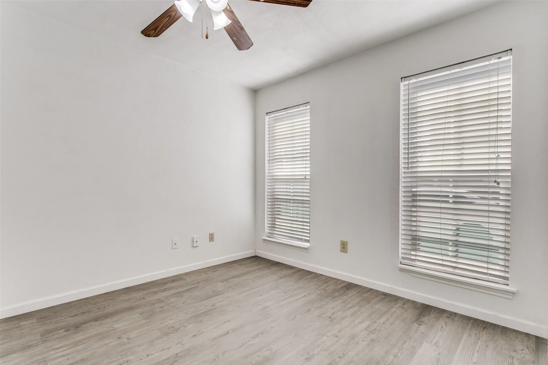 Room with wood-finish flooring, white walls, and white baseboards