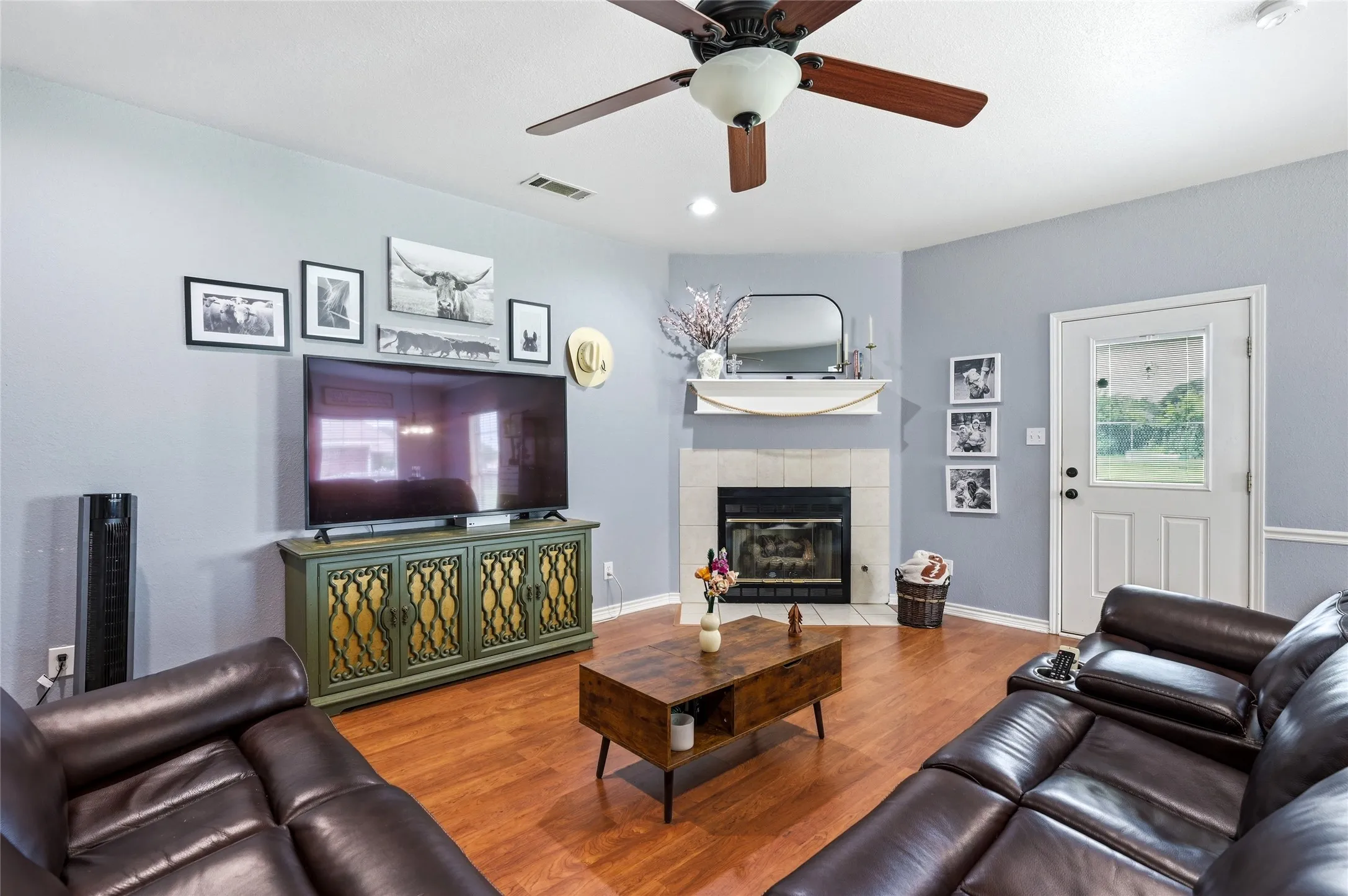 Living area featuring wood-finish flooring, a corner fireplace with a tile surround and mantel, and a ceiling fan