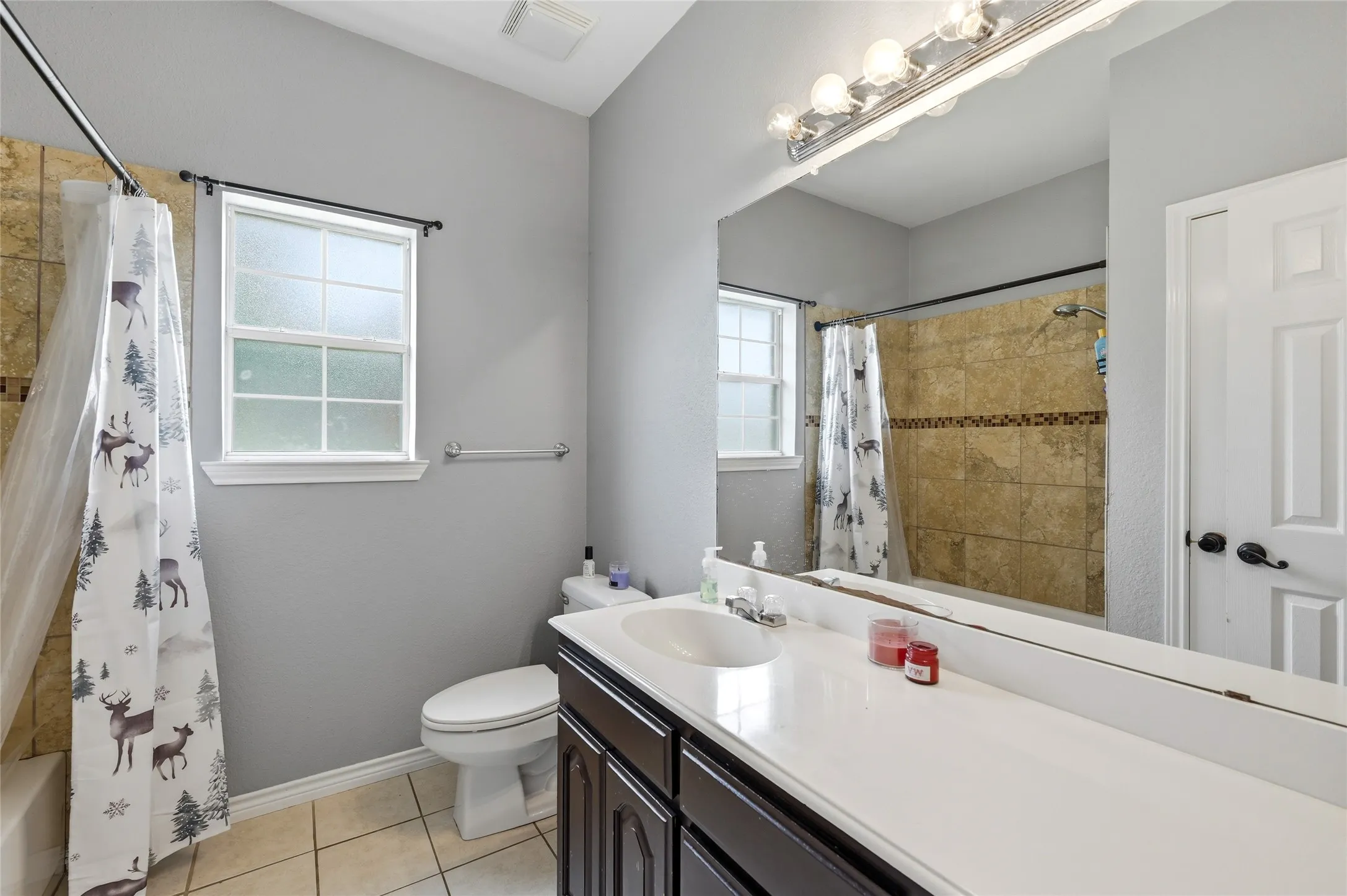 Bathroom featuring a built-in vanity with a white countertop and dark wood cabinetry, a large wall-mounted mirror, a tiled shower with a tub, a white commode, and a window with privacy glass