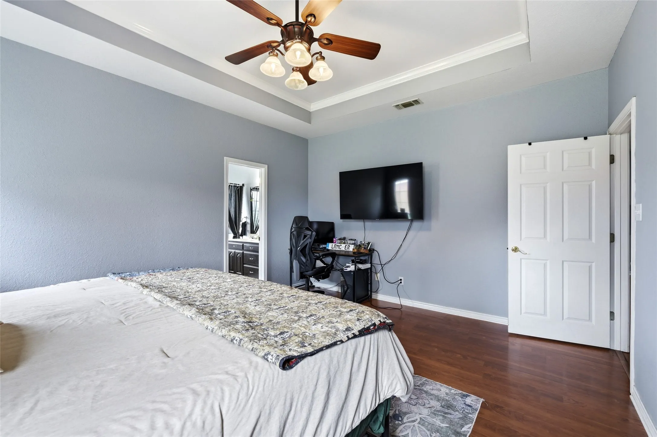 Tray ceiling with crown molding, ceiling fan with light fixture, wood-finish flooring, and a flat-panel door