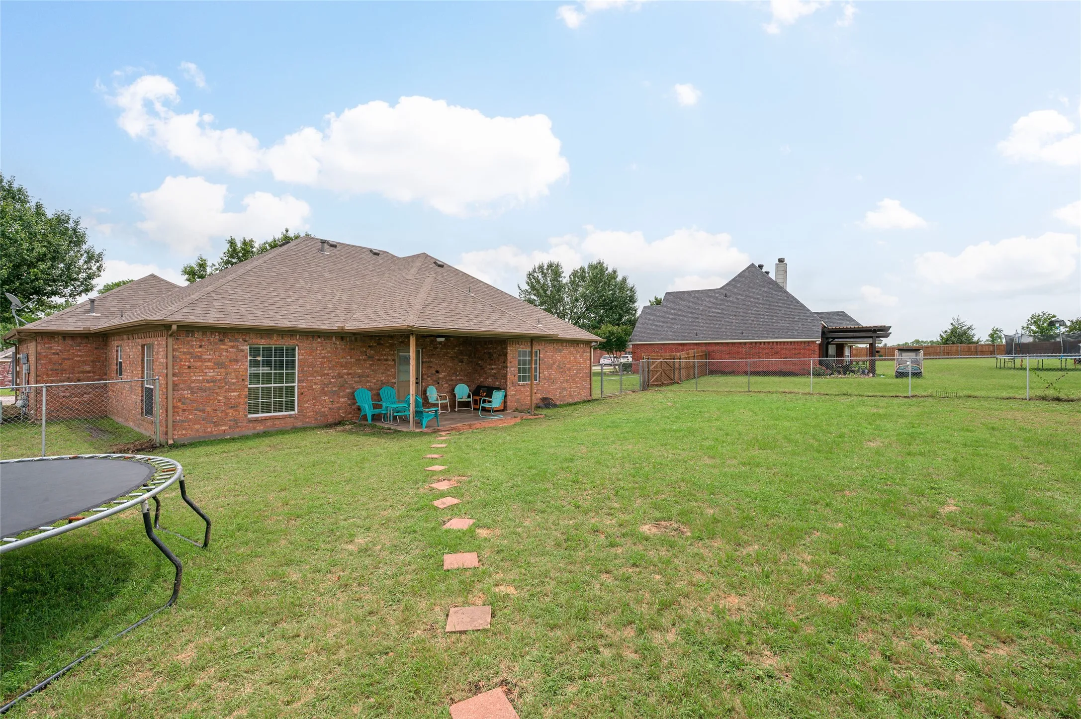 Expansive backyard featuring a manicured lawn, a chain-link fence, and a stepping stone pathway