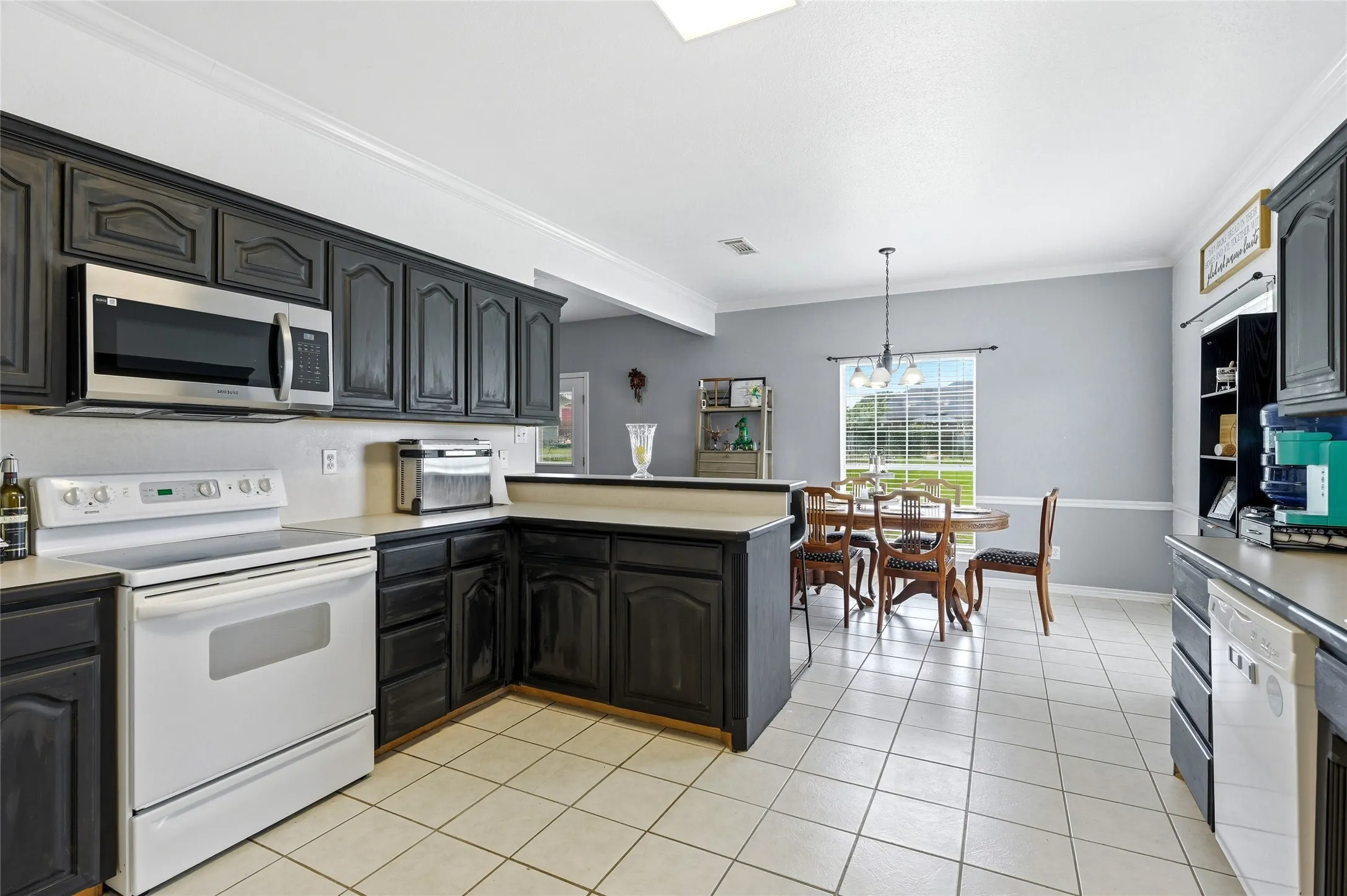 Kitchen featuring dark cabinetry, stainless steel microwave, white range, tile flooring, and a breakfast bar