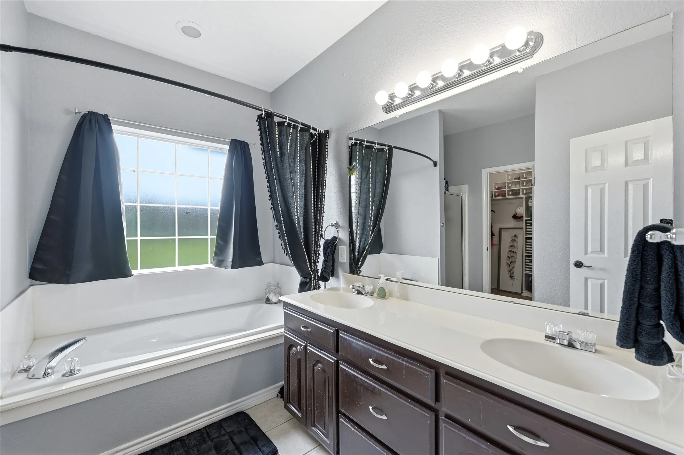 Bathroom featuring a built-in tub with a window, a double vanity with an integrated countertop, and a large mirror with overhead lighting