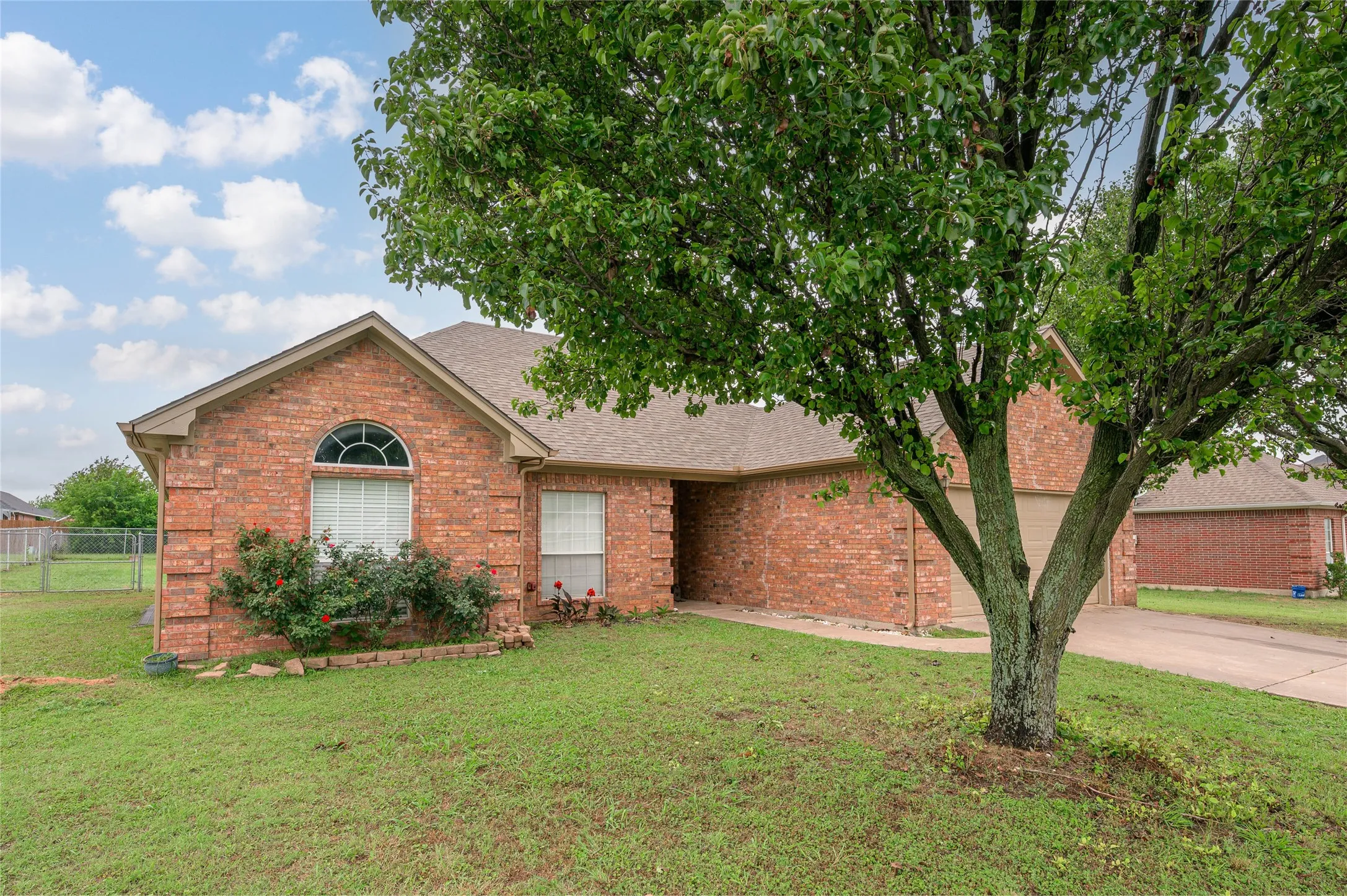 Brick exterior residence featuring a gabled roofline, an arched transom window, a concrete driveway, and mature landscaping