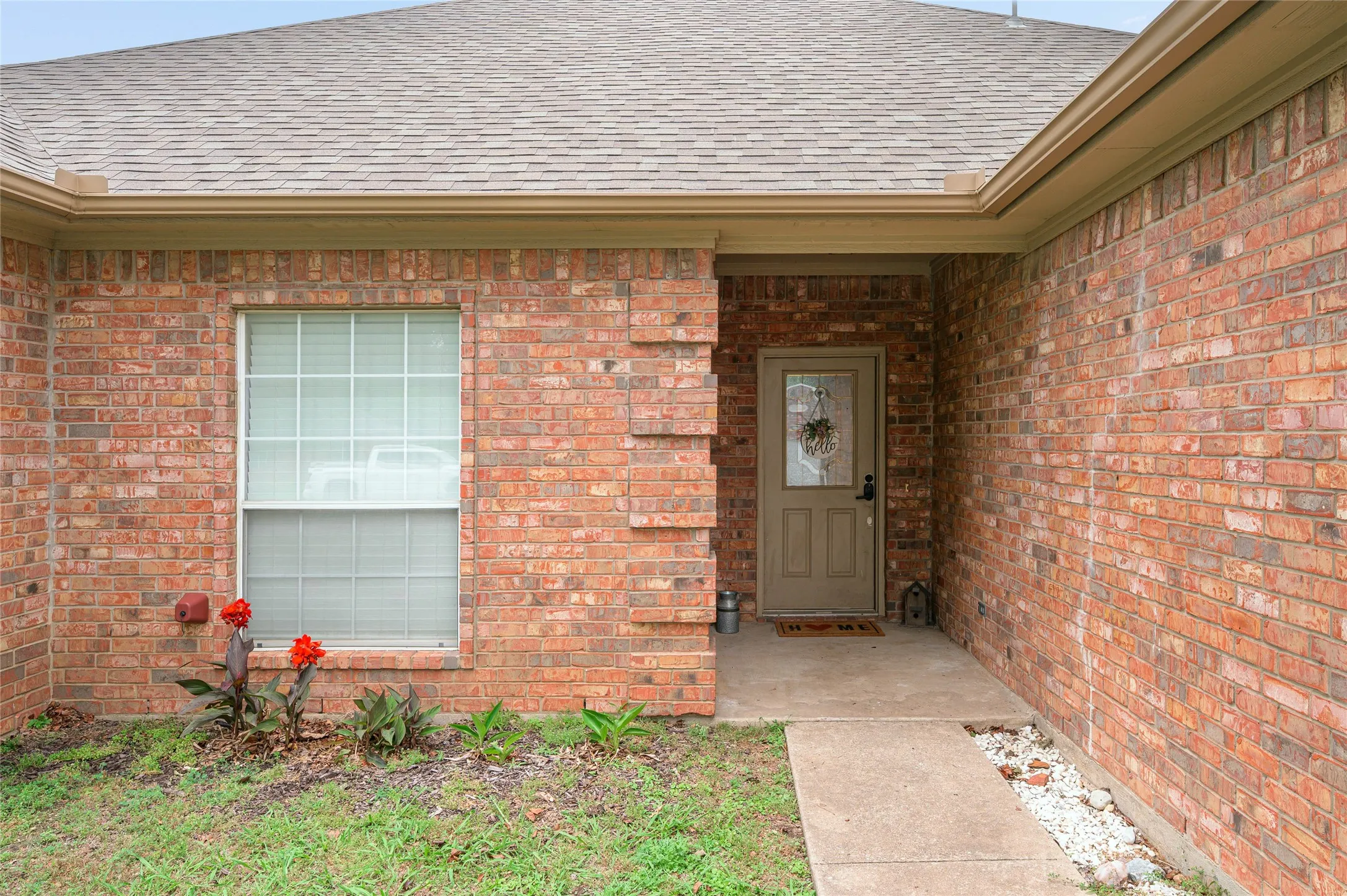 Brick exterior featuring a covered entry, a paneled front door with a decorative glass insert, and a white grid window