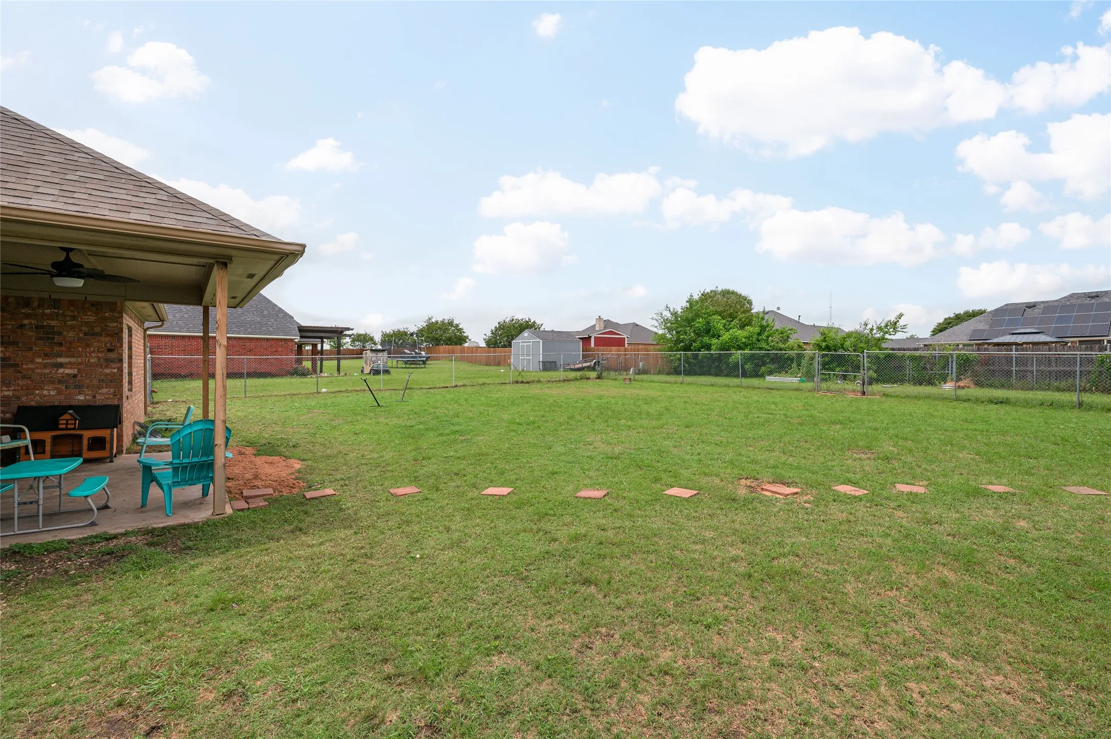 Spacious backyard featuring a covered patio with a ceiling fan, a manicured lawn, and perimeter chain link fencing