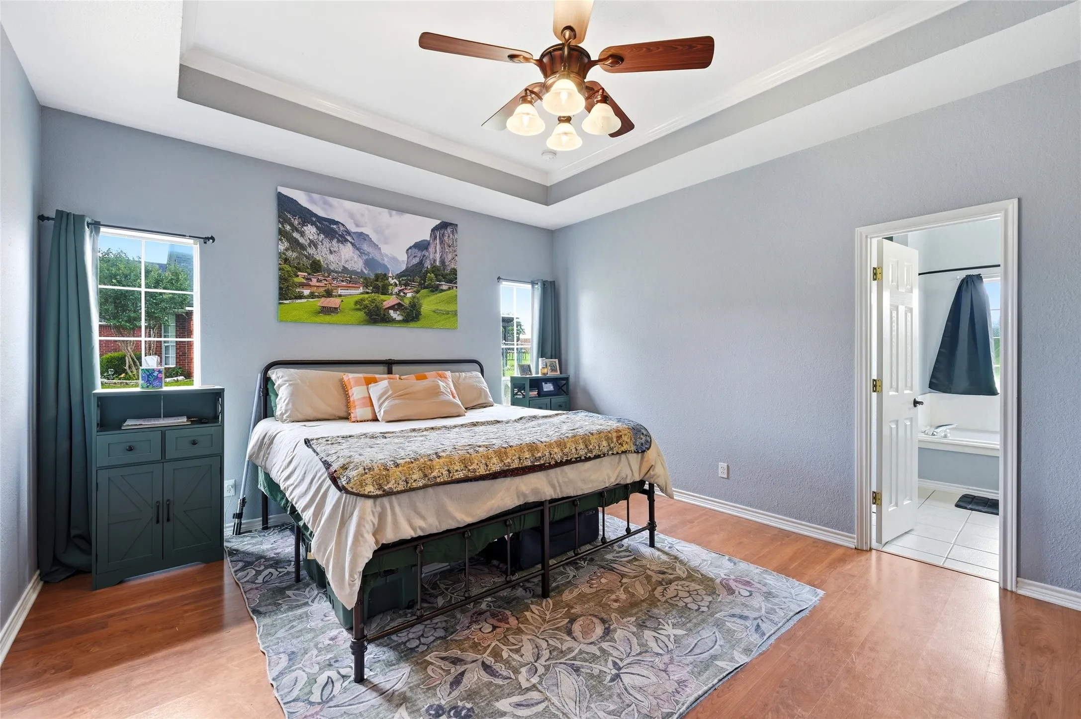 Spacious bedroom featuring a tray ceiling, wood-finish flooring, and crown molding