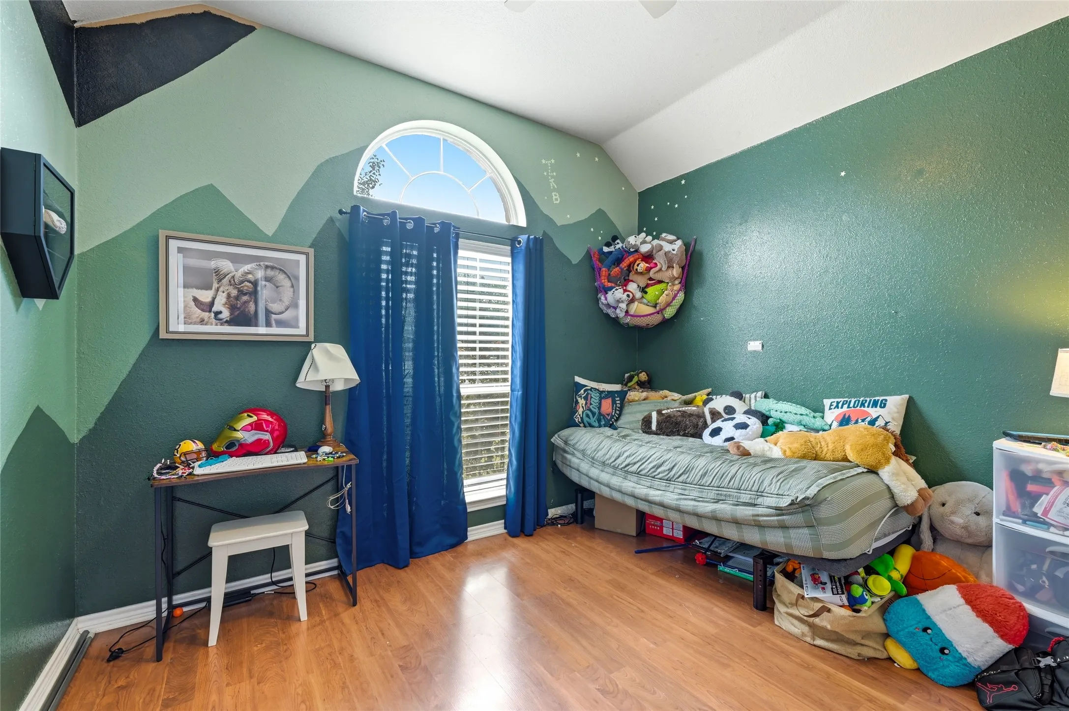 Room featuring wood-finish flooring, a tall arched window with blinds, and a textured wall finish