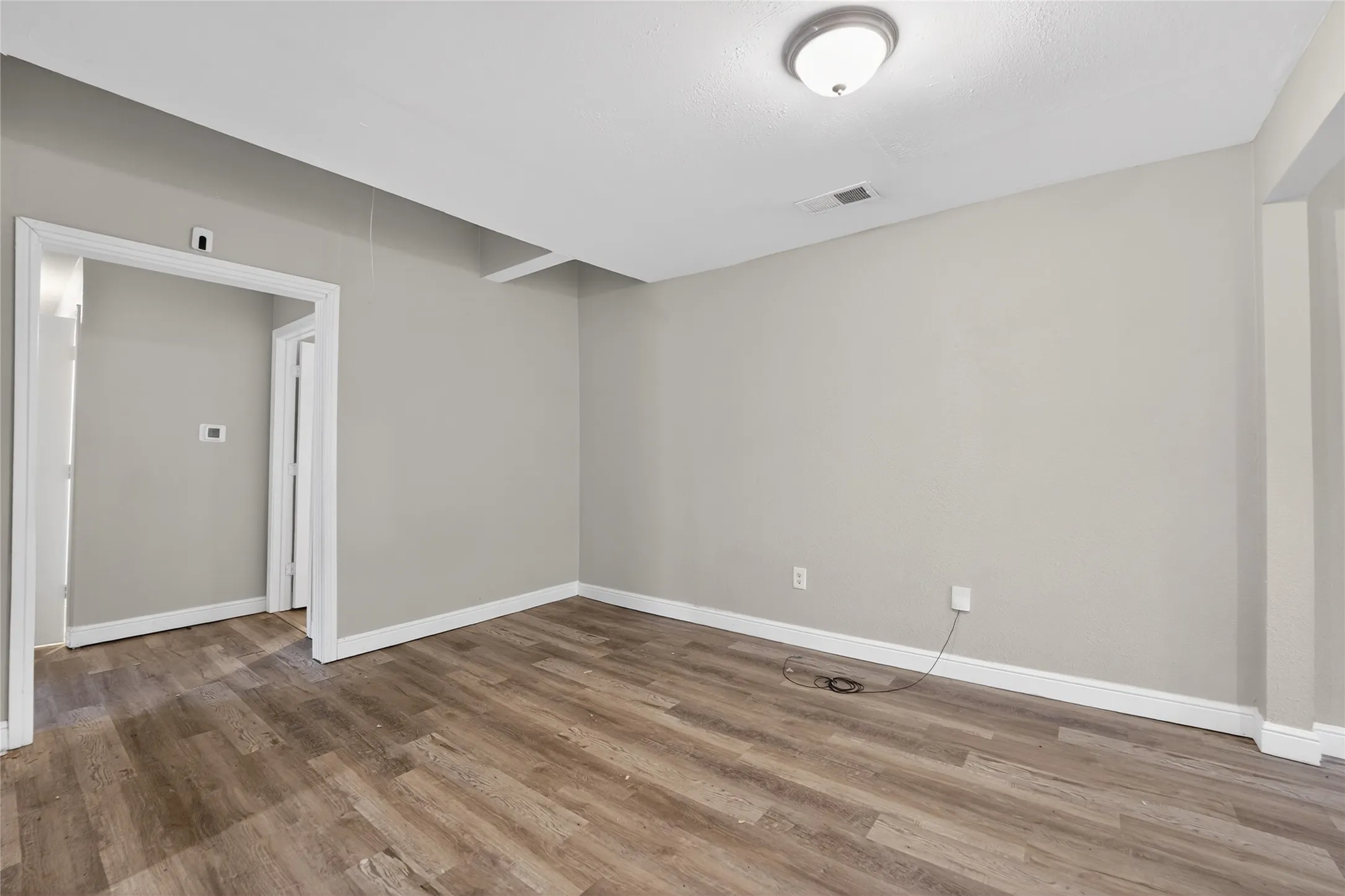 Spacious room with wood-finish flooring, light grey walls, white trim, and a flush-mount ceiling light fixture