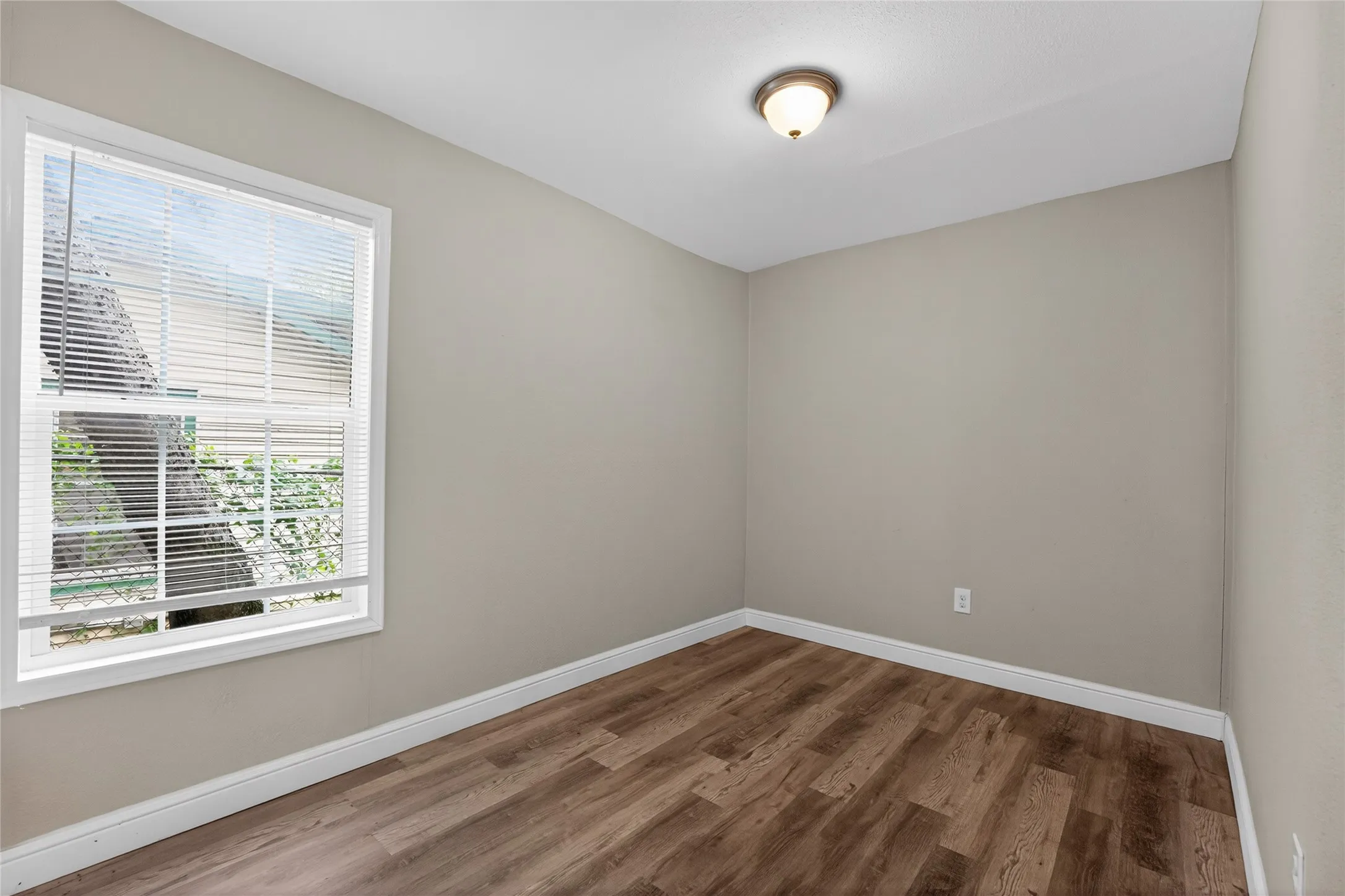 Room featuring a single-pane window with white blinds, wood-finish flooring, neutral wall tones, and white baseboards