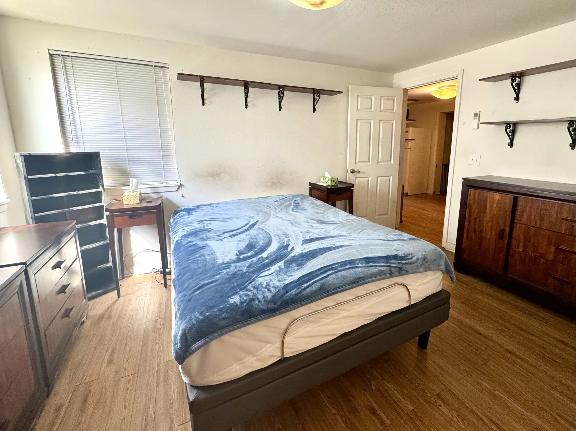 Primary Bedroom: Wood-finish flooring throughout the room, complemented by a window with blinds providing natural light