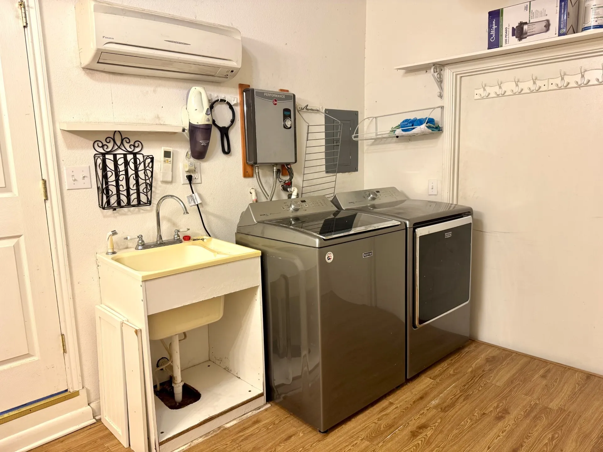 Laundry is OPEN to Primary Bath: Features utility sink, wood-finish flooring, wall-mounted mini-split unit, and tankless water heater