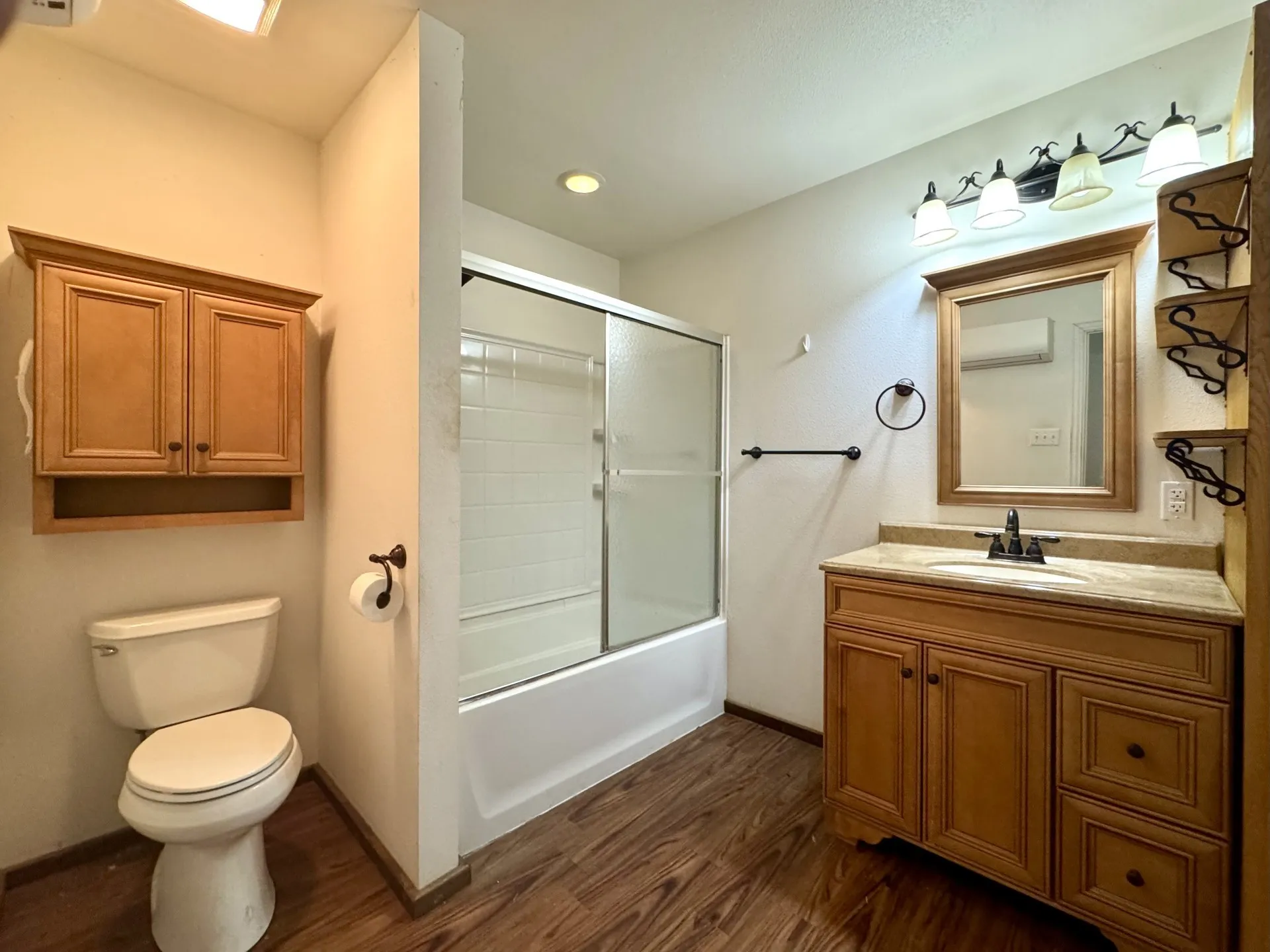 Full HALL Bathroom featuring a wood-finish floor, single vanity with a stone countertop, built-in shelving, and a combination shower/tub with sliding glass doors