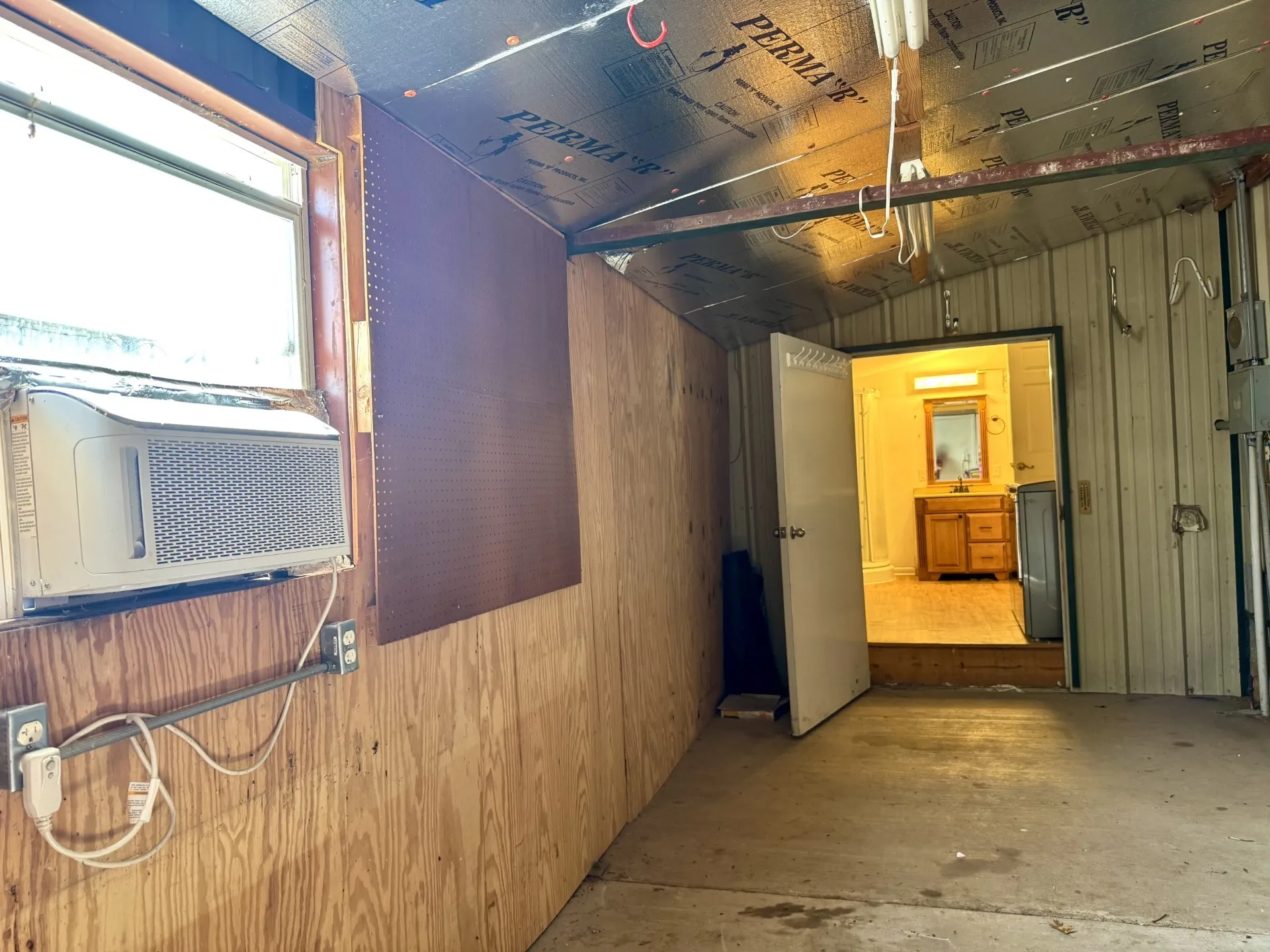 Workshop OPENS to Primary Bath: Electric, Window AC Unit, plywood wall paneling, metal walls, and concrete flooring