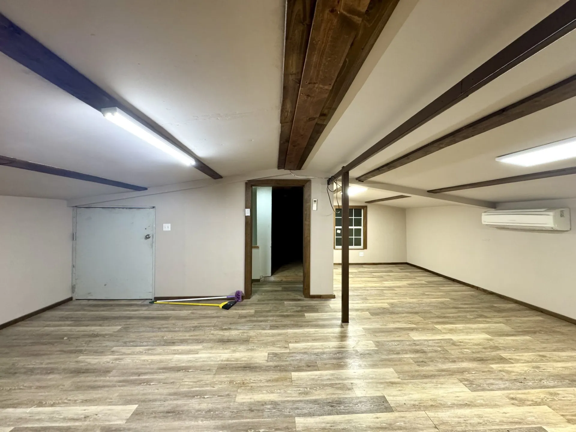 UPSTAIRS BONUS Room featuring wood-finish flooring, exposed ceiling beams, and a wall-mounted air conditioning unit - OPENS to Unfinished Storage Room.