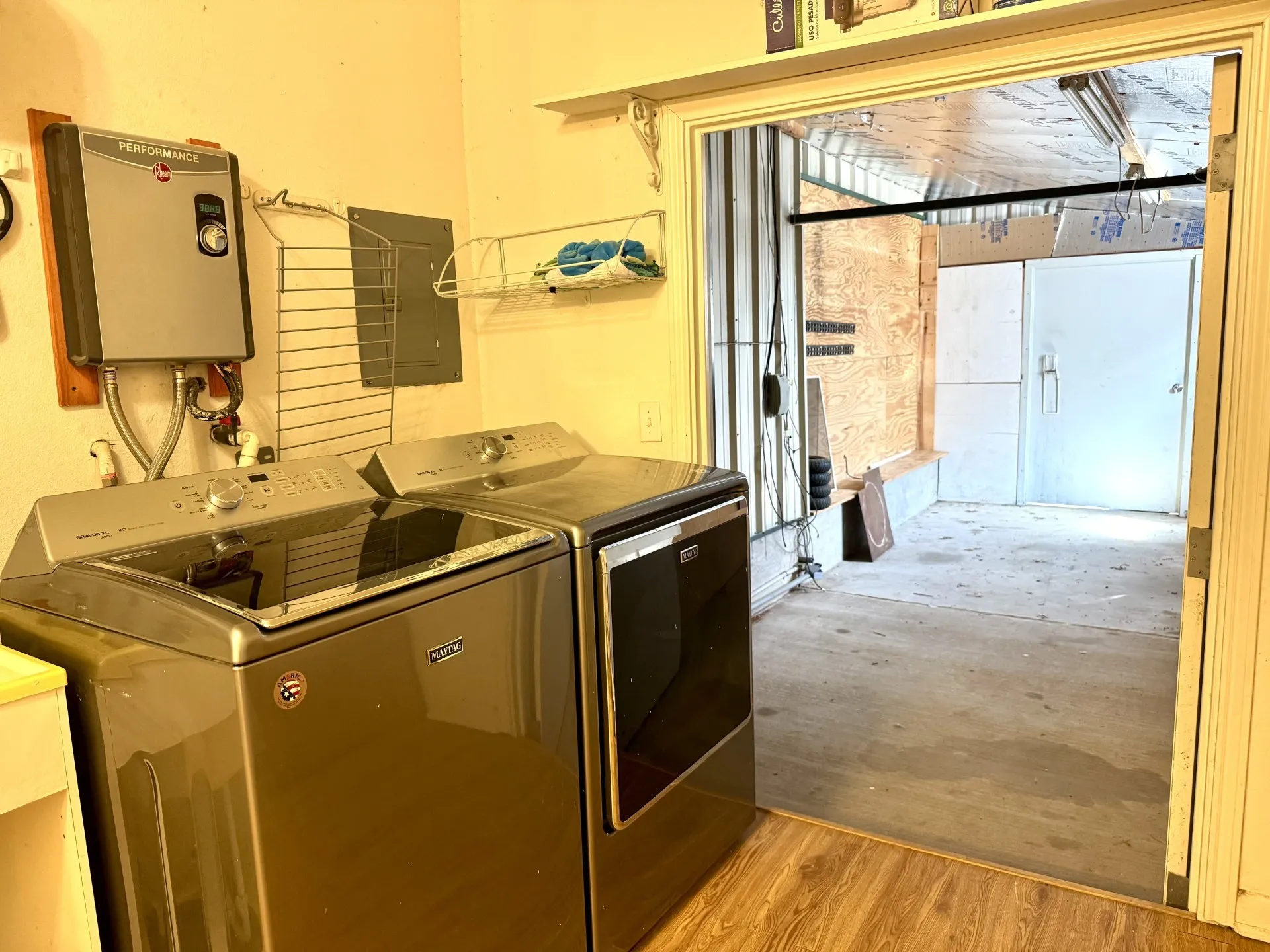 Utility area with a wall-mounted tankless water heater, wood-finish flooring, and a concrete-floored storage space