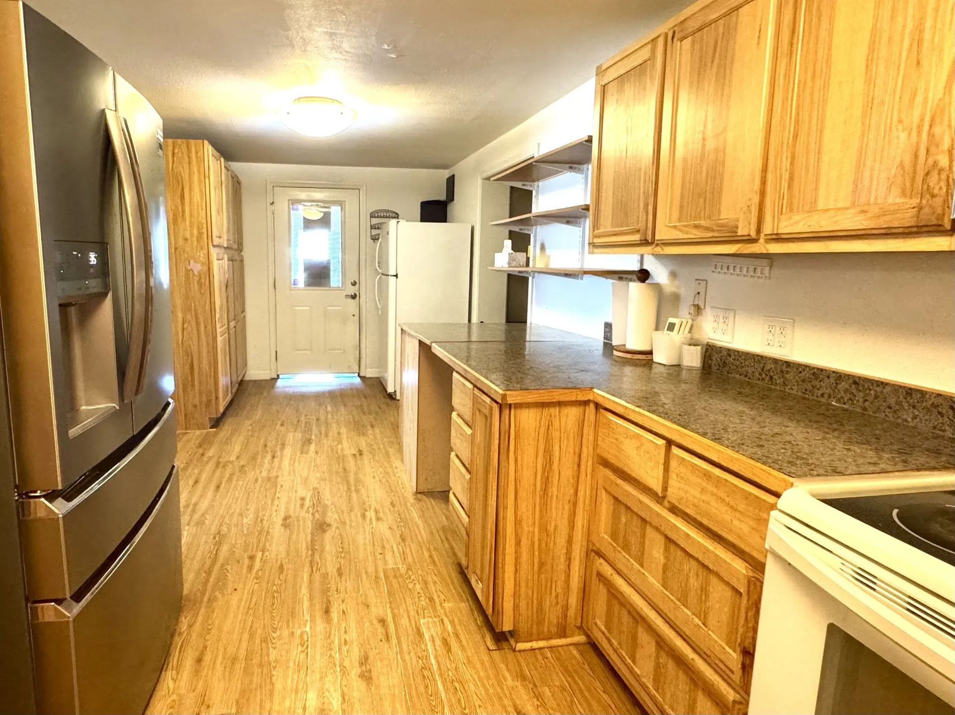 Kitchen featuring wood-finish flooring, extensive wood cabinetry, mottled countertops, and a white door with a window pane