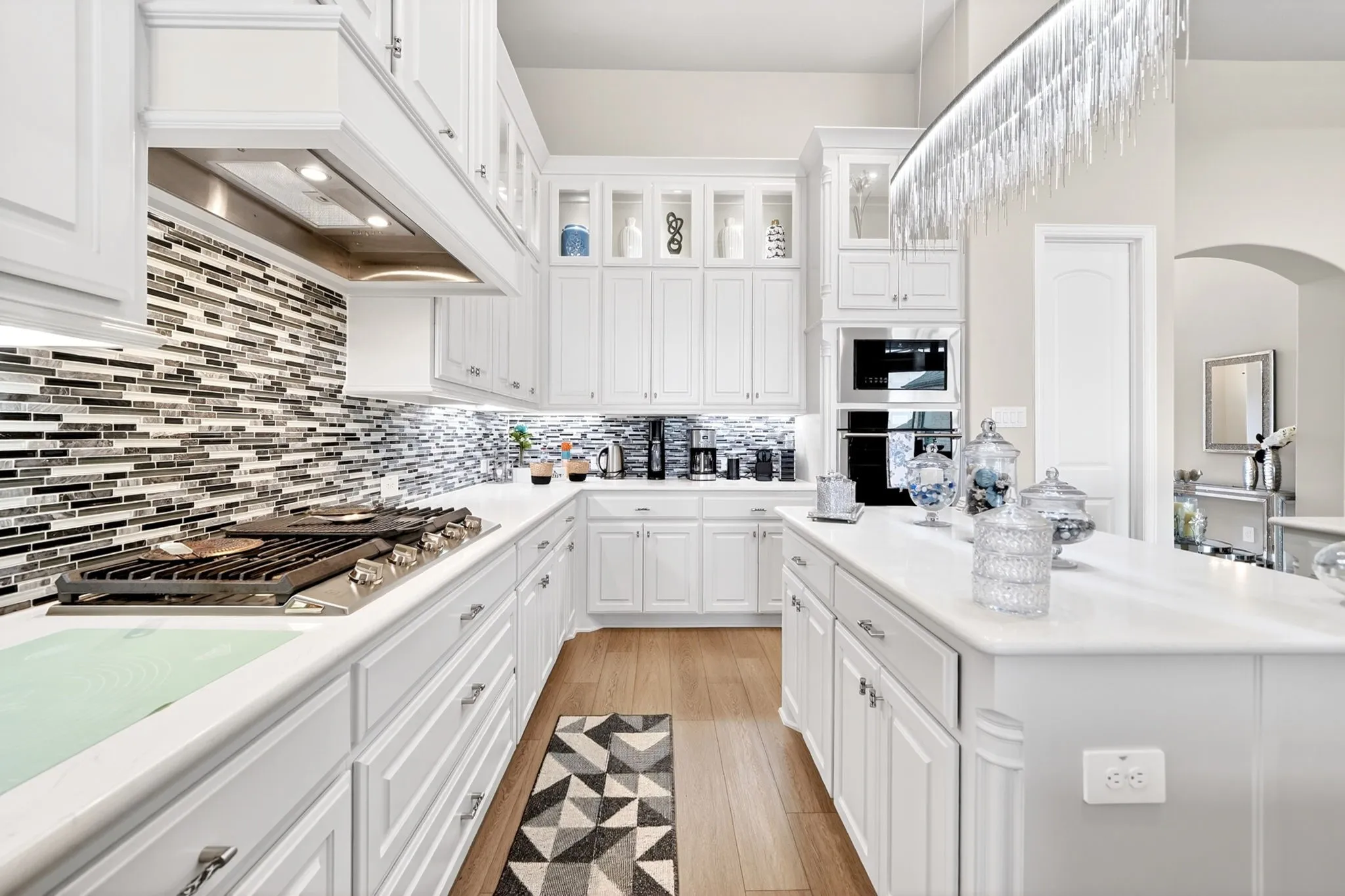 Kitchen featuring white cabinetry, wood-finish flooring, an extensive island, a built-in oven, and a contemporary linear chandelier